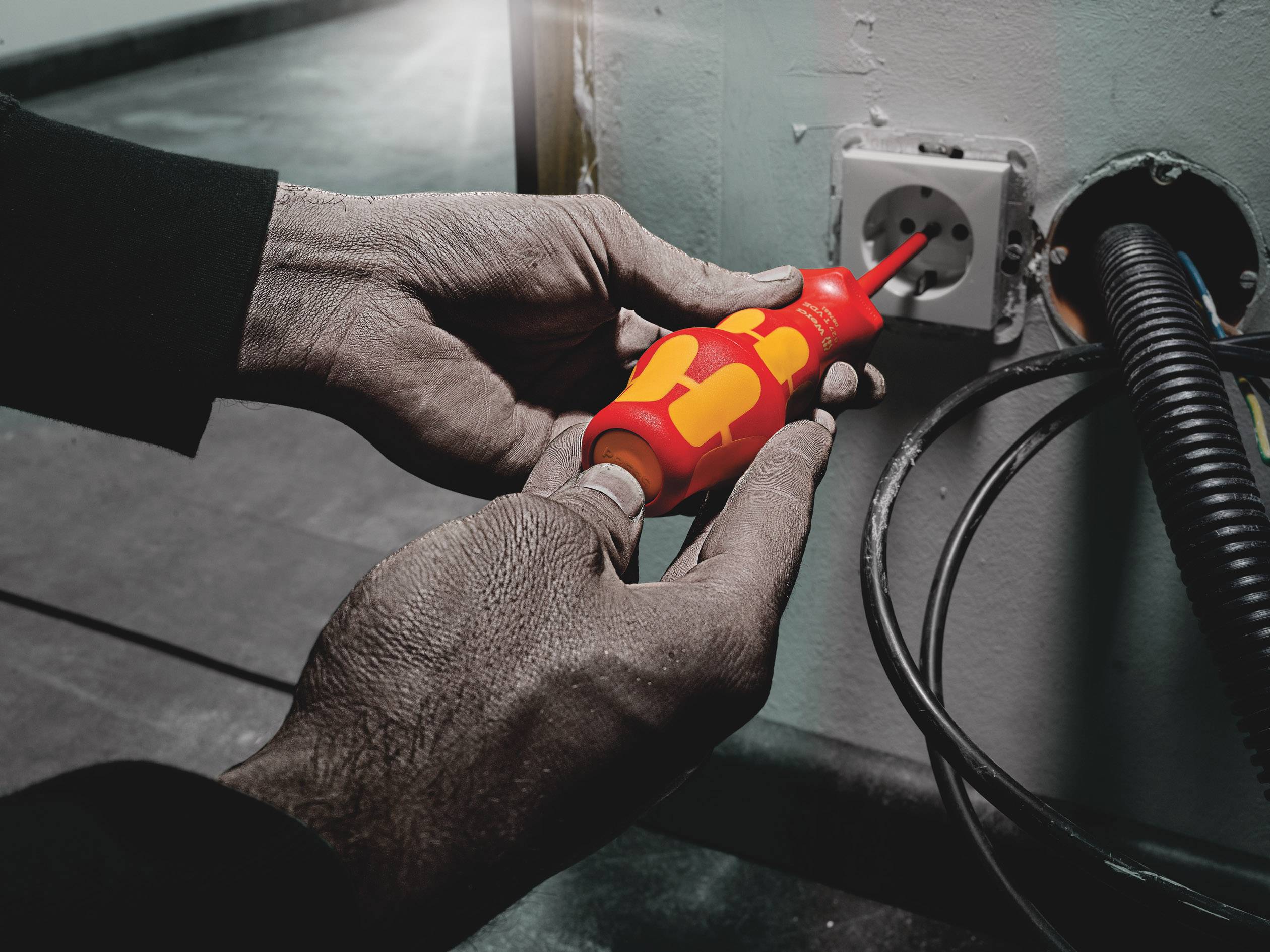 Eine Person testet eine Steckdose mit einem Spannungsprüfer. Kabel führen zu der Steckdose.