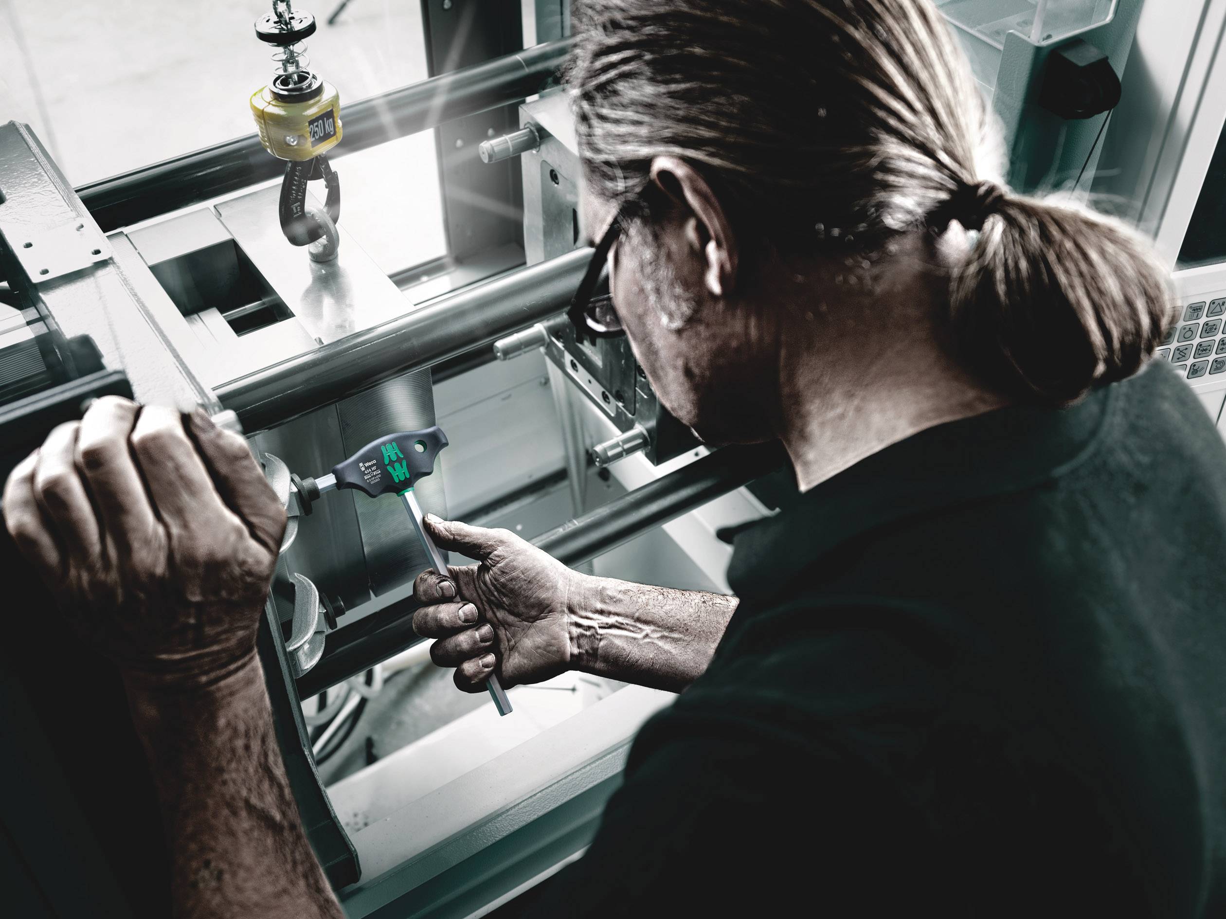 Ein Mann misst ein Metallteil mit einem digitalen Messschieber in einer industriellen Werkstattumgebung.