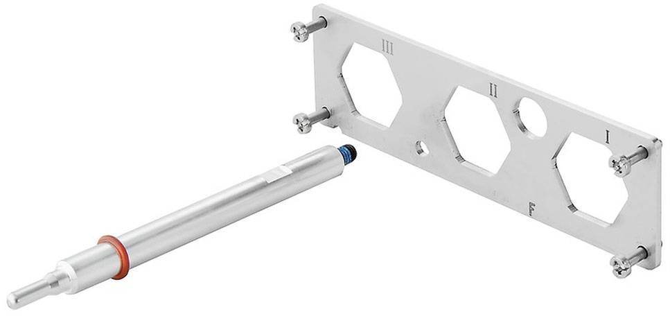 Ein silberner Stift neben einer Metallplatte mit drei sechseckigen Öffnungen, nummeriert mit 'III', 'I', 'II'.