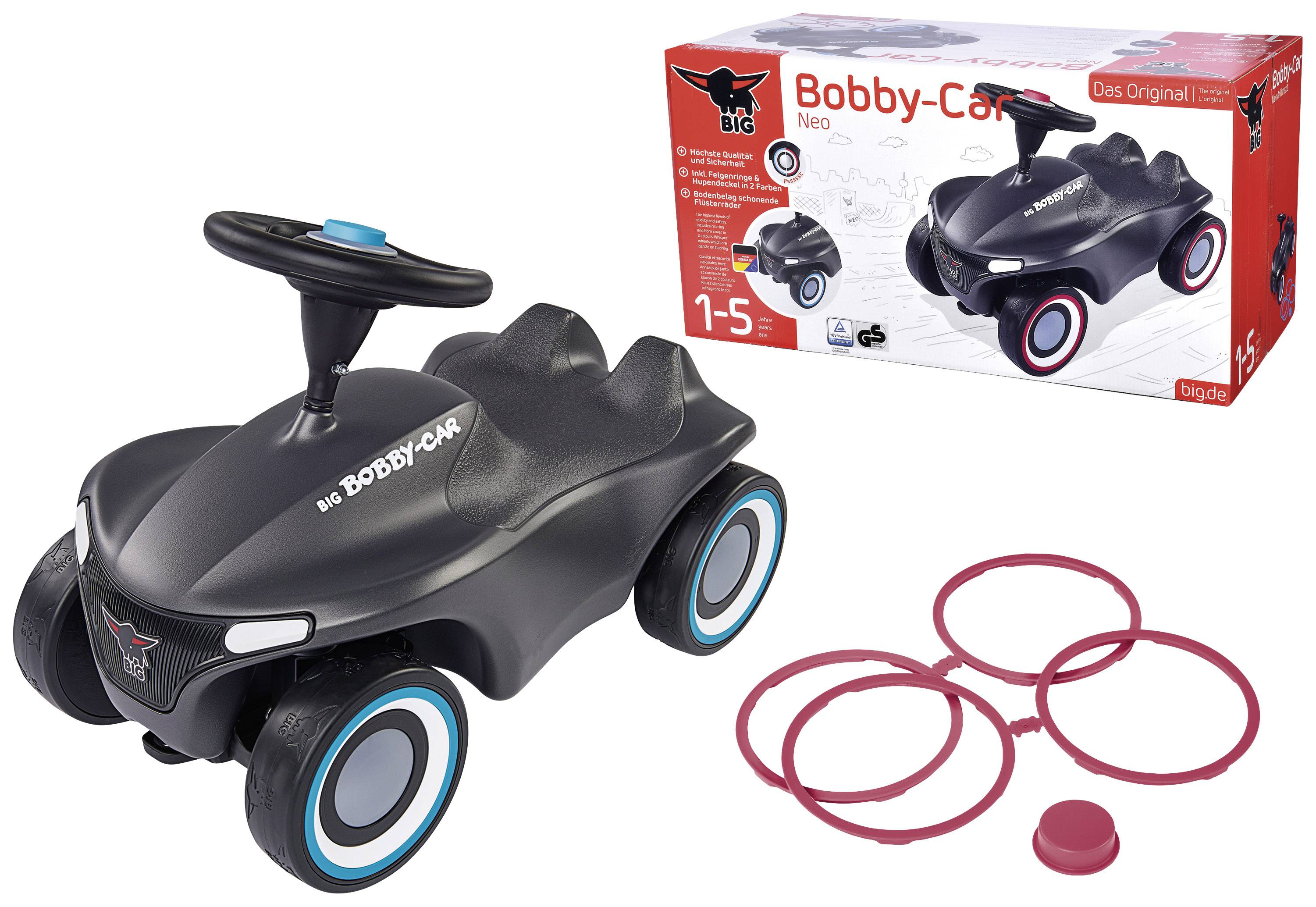 Kinderspielzeugauto 'Bobby-Car Neo' in Schwarz mit blauen Reifen, rotem Lenkknopf und Zubehör. Verpackung im Hintergrund zeigt das Auto.