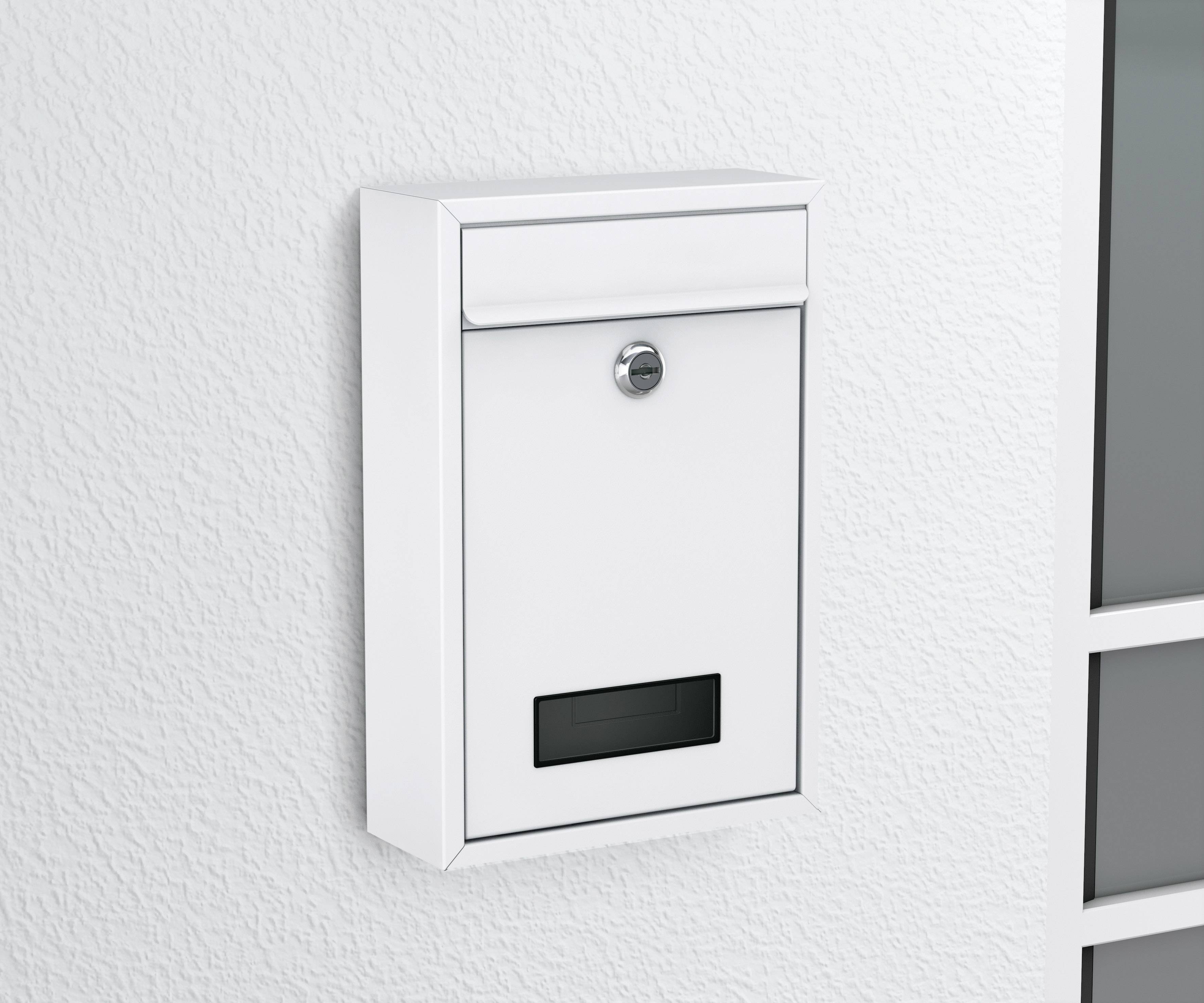 Ein weißer Briefkasten mit einem Schloss hängt an einer weißen Wand neben einem Fenster.