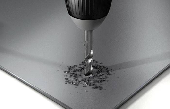 Ein Bohrer durchdringt ein Metallblech, umgeben von Metallspänen.