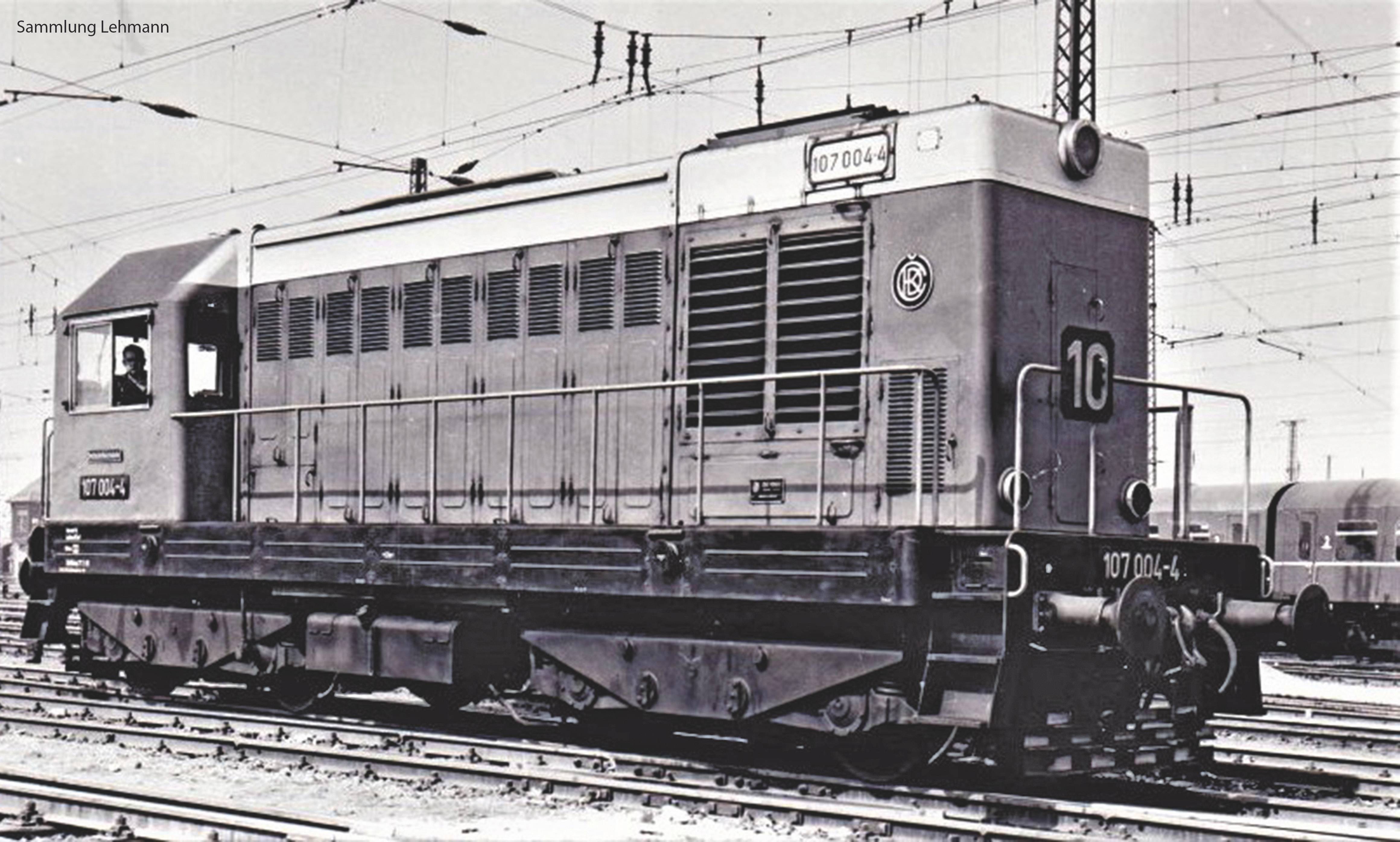 Schwarz-weiß-Foto einer historischen Lok mit der Aufschrift '107 004-4', auf Gleisen stehend. Oberleitungen und Weichen im Hintergrund.