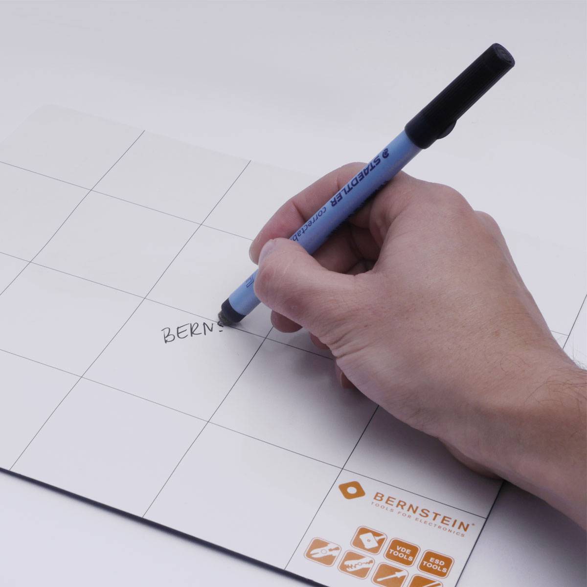Eine Hand schreibt mit einem blauen Stift auf eine weiße Schreibtafel, die das Wort 'BERNSTEIN' zeigt. Im Hintergrund sind Symbole zu sehen.
