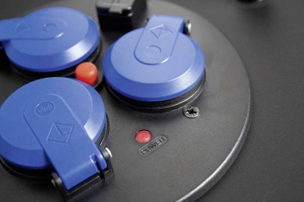 Drei blaue Abdeckungen auf einer schwarzen Platte, zwei rote Knöpfe und eine Schraube.