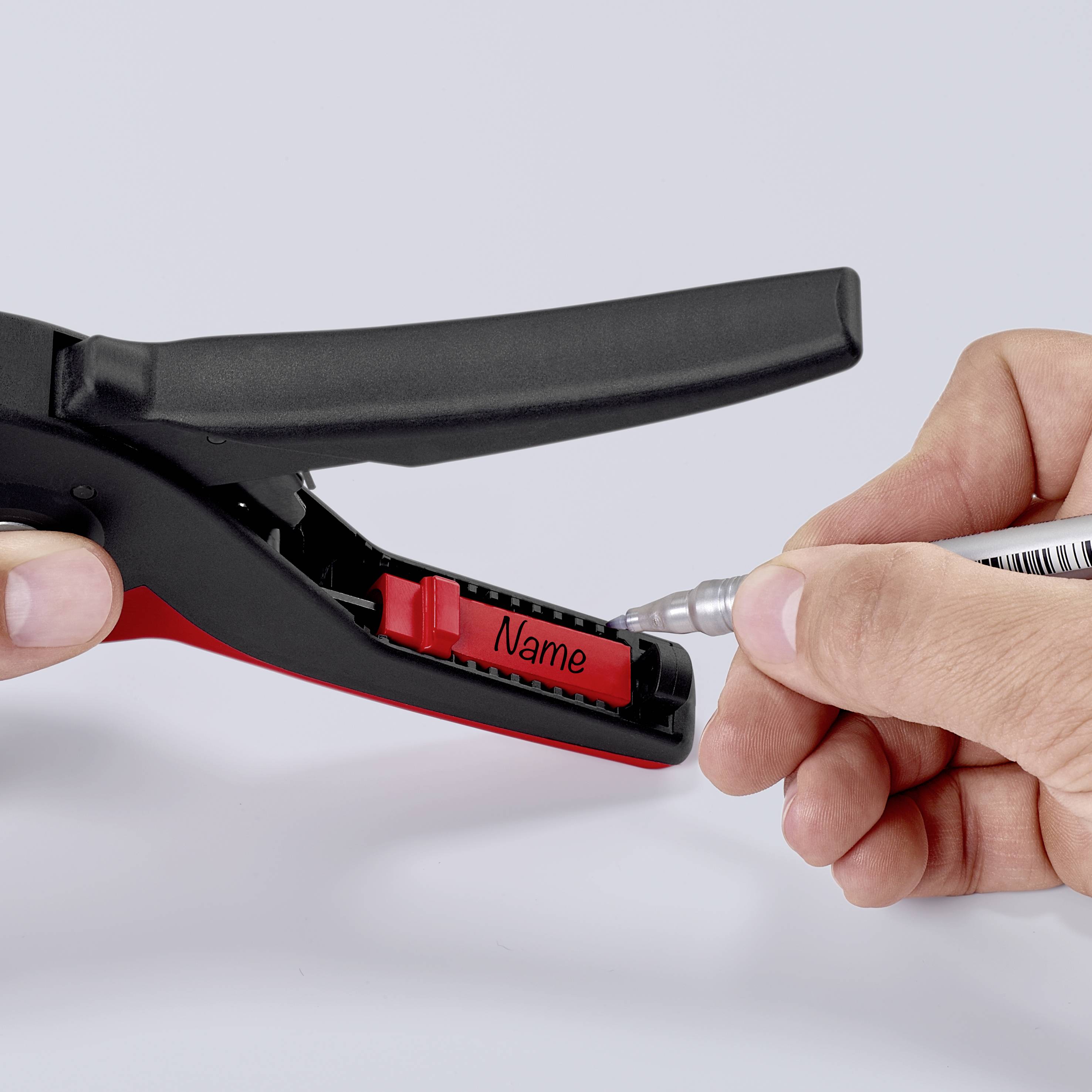 Hand trägt mit einem Stift einen Namen auf ein rotes Namensschild ein, das in einem schwarzen Halter befestigt ist.