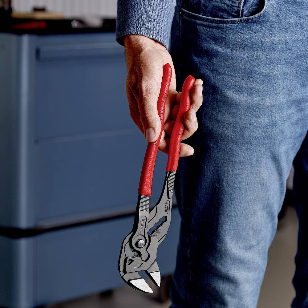 Eine Person hält eine rote Rohrzange in der rechten Hand. Im Hintergrund ist unscharf ein blauer Werkzeugschrank erkennbar.