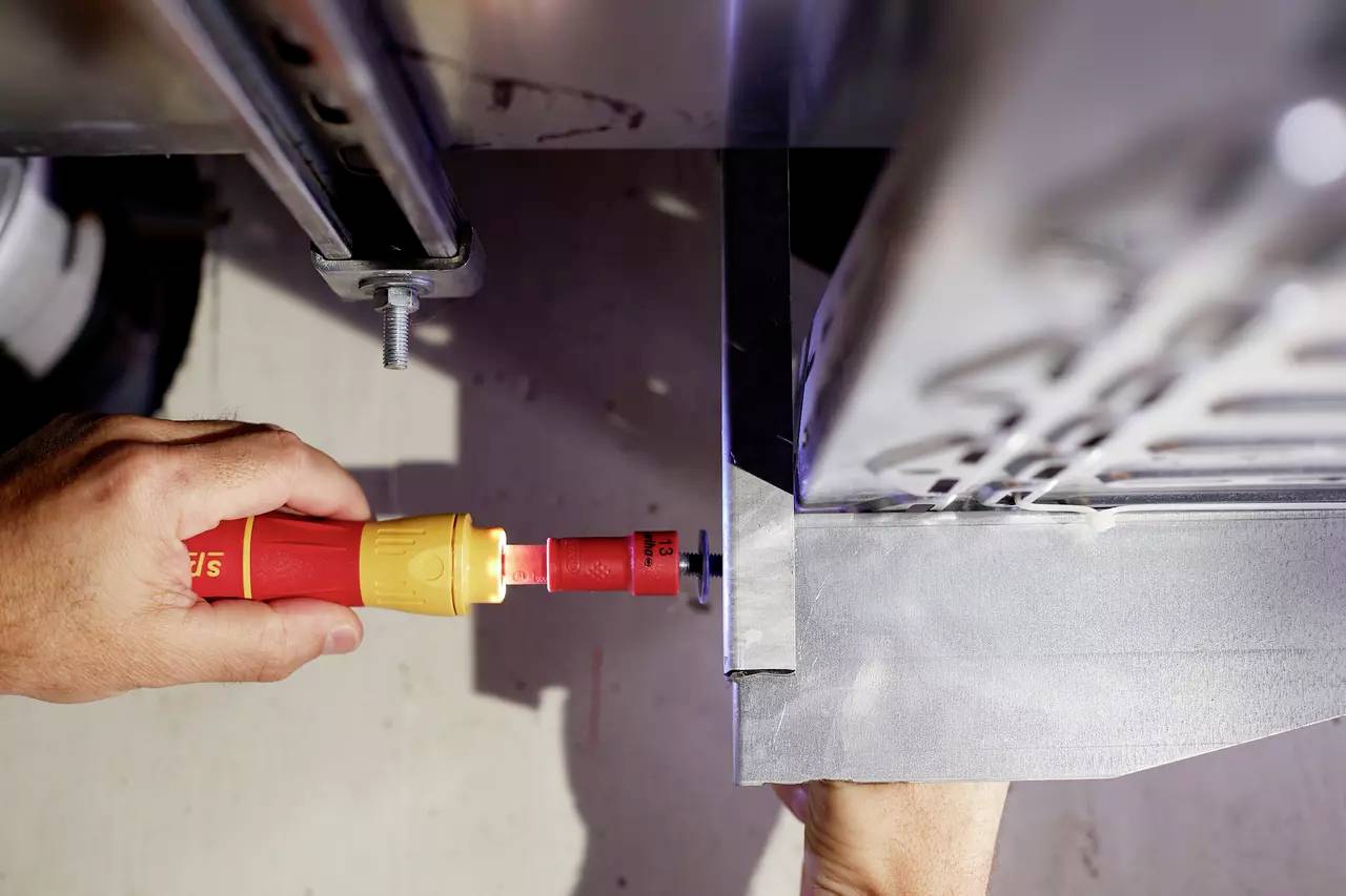 Eine Hand mit Schraubendreher befestigt eine Metallplatte an einem Rahmen. Werkzeug in Aktion nahe einer Maschinenstruktur.