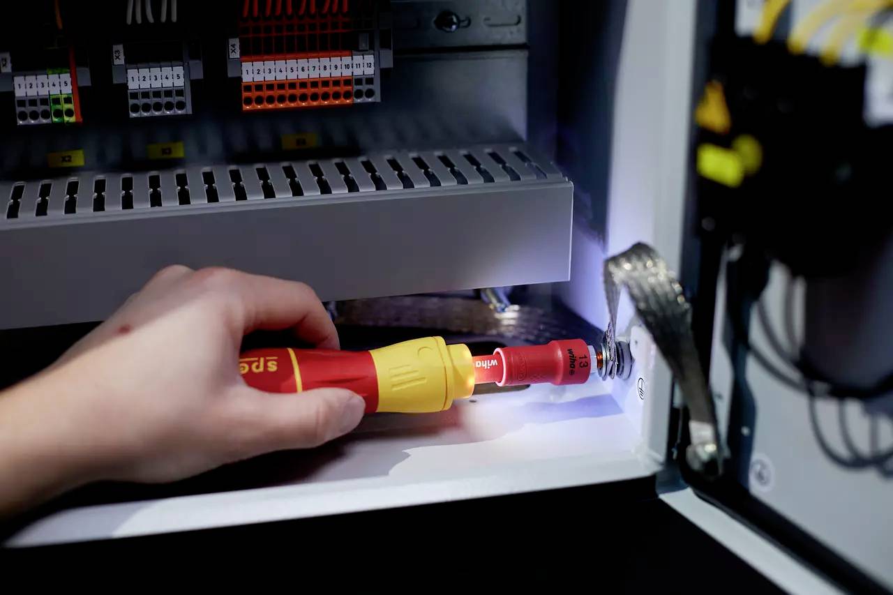 Hand mit Schraubendreher befestigt eine Schraube in einem elektrischen Schaltschrank. Kabel und Anschlüsse sind sichtbar.