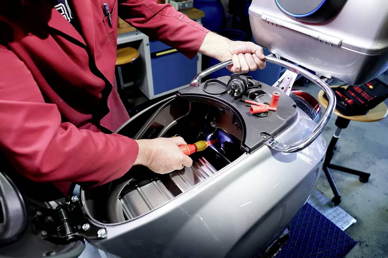 Eine Person arbeitet an einem Elektroroller. Sie verwendet Werkzeug, um den Motorraum im hinteren Teil des Rollers zu inspizieren.