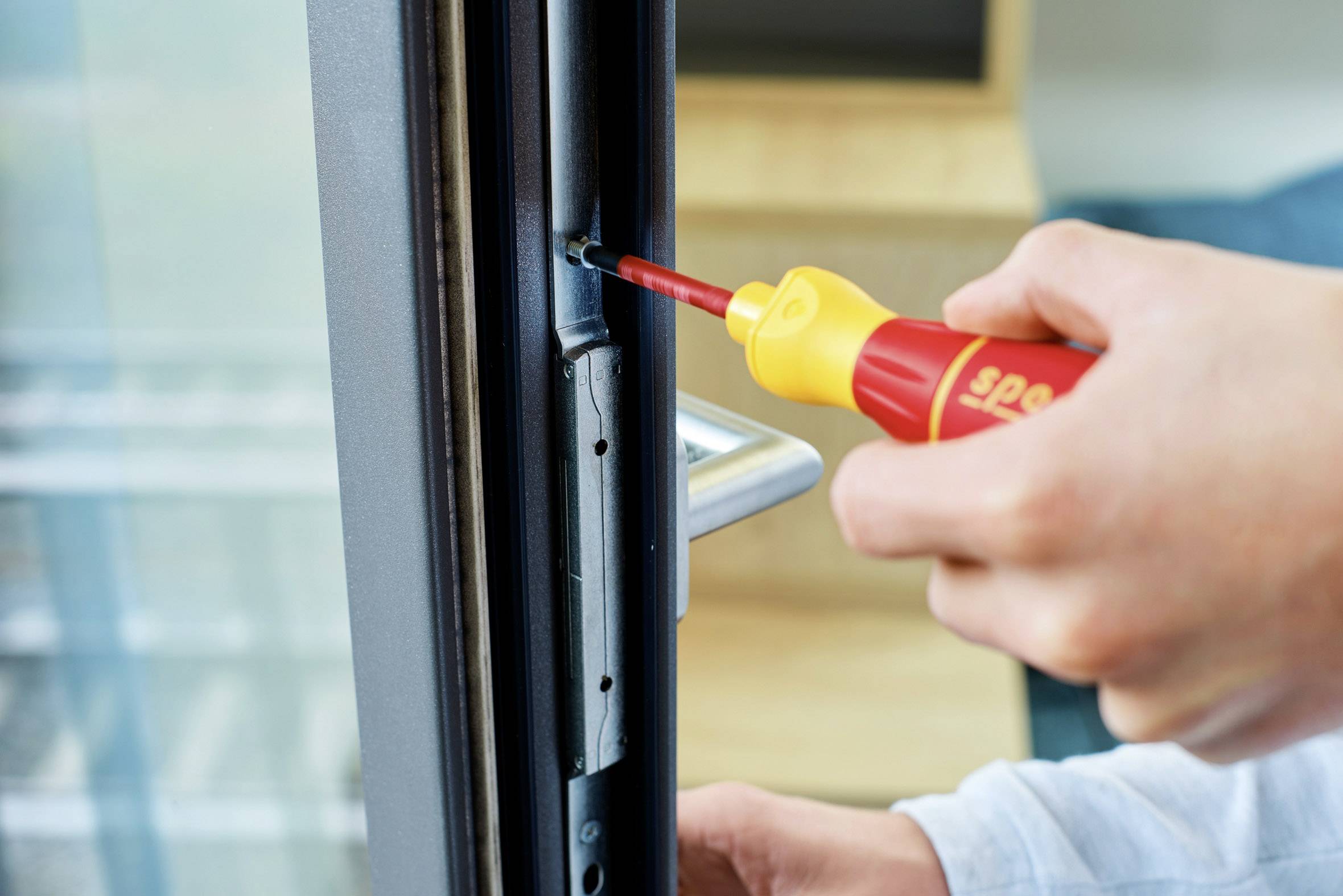 Eine Person zieht mit einem Schraubendreher eine Schraube an der Kante eines Fensters fest, um es zu reparieren oder anzupassen.