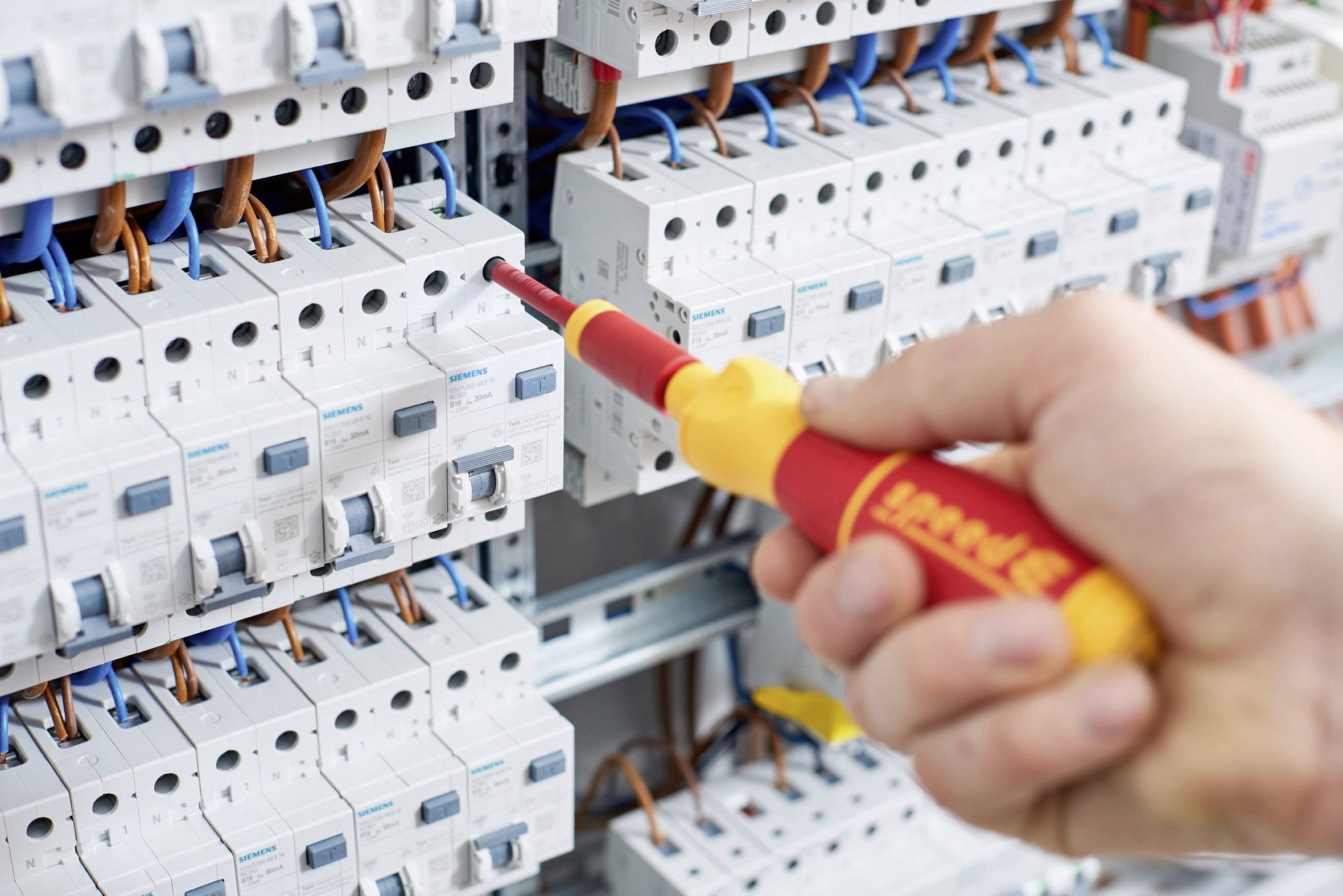Eine Hand arbeitet mit einem isolierten Schraubendreher an einem Sicherungskasten, um elektrische Leitungen zu überprüfen oder zu justieren.