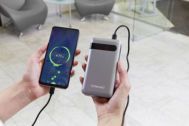 Eine Person hält ein Smartphone, das über ein Kabel mit einer tragbaren Powerbank verbunden ist. Das Smartphone zeigt einen Ladevorgang an.