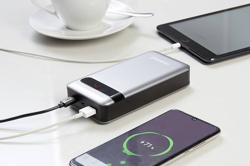 Eine Powerbank lädt zwei Geräte auf einem Tisch auf: ein Smartphone mit 71% Ladung und ein Tablet. Im Hintergrund eine Tasse.