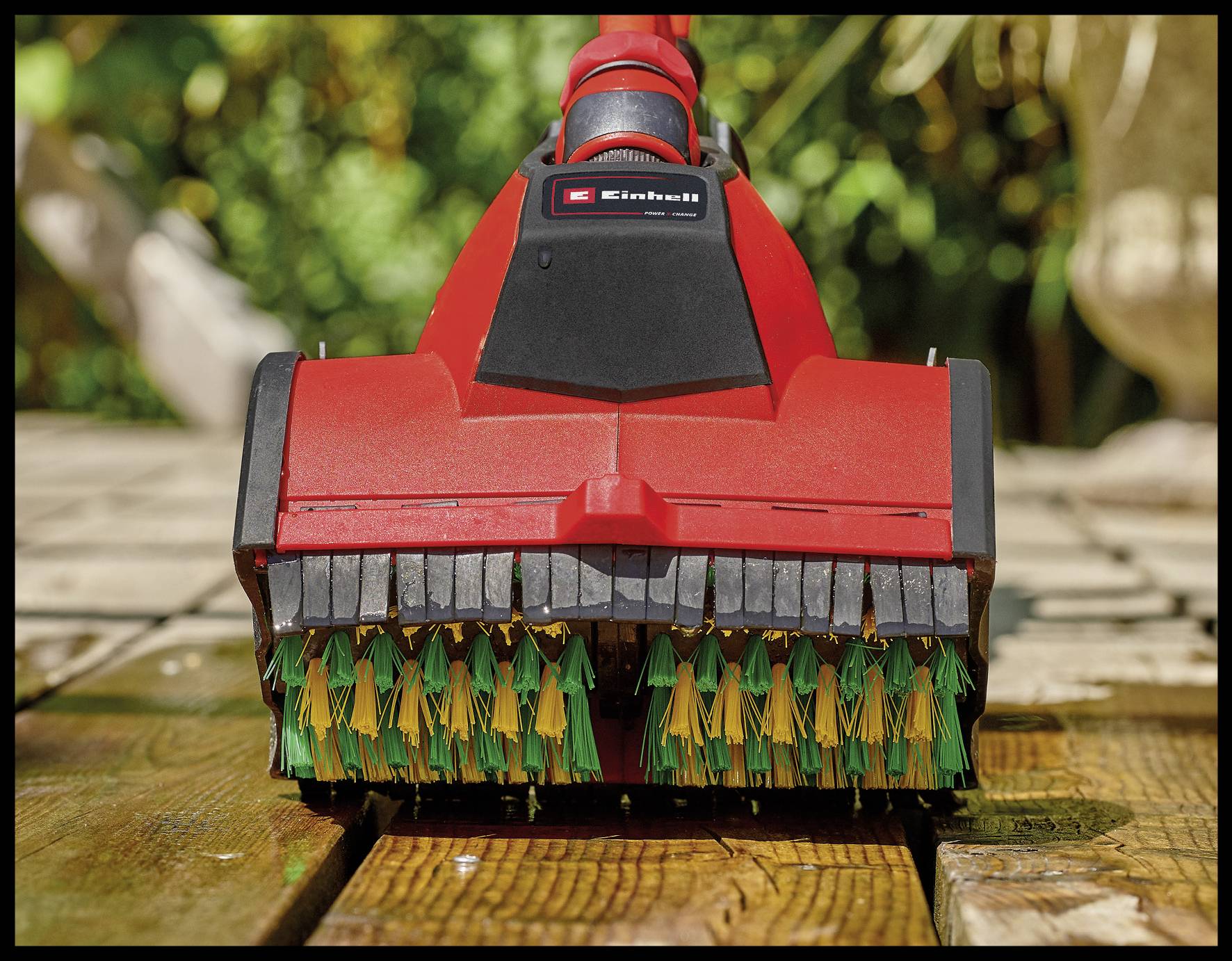 Roter elektrischer Bodenreiniger mit rotierenden Bürsten, steht auf einer hölzernen Terrasse. Im Hintergrund Pflanzen im Sonnenlicht.