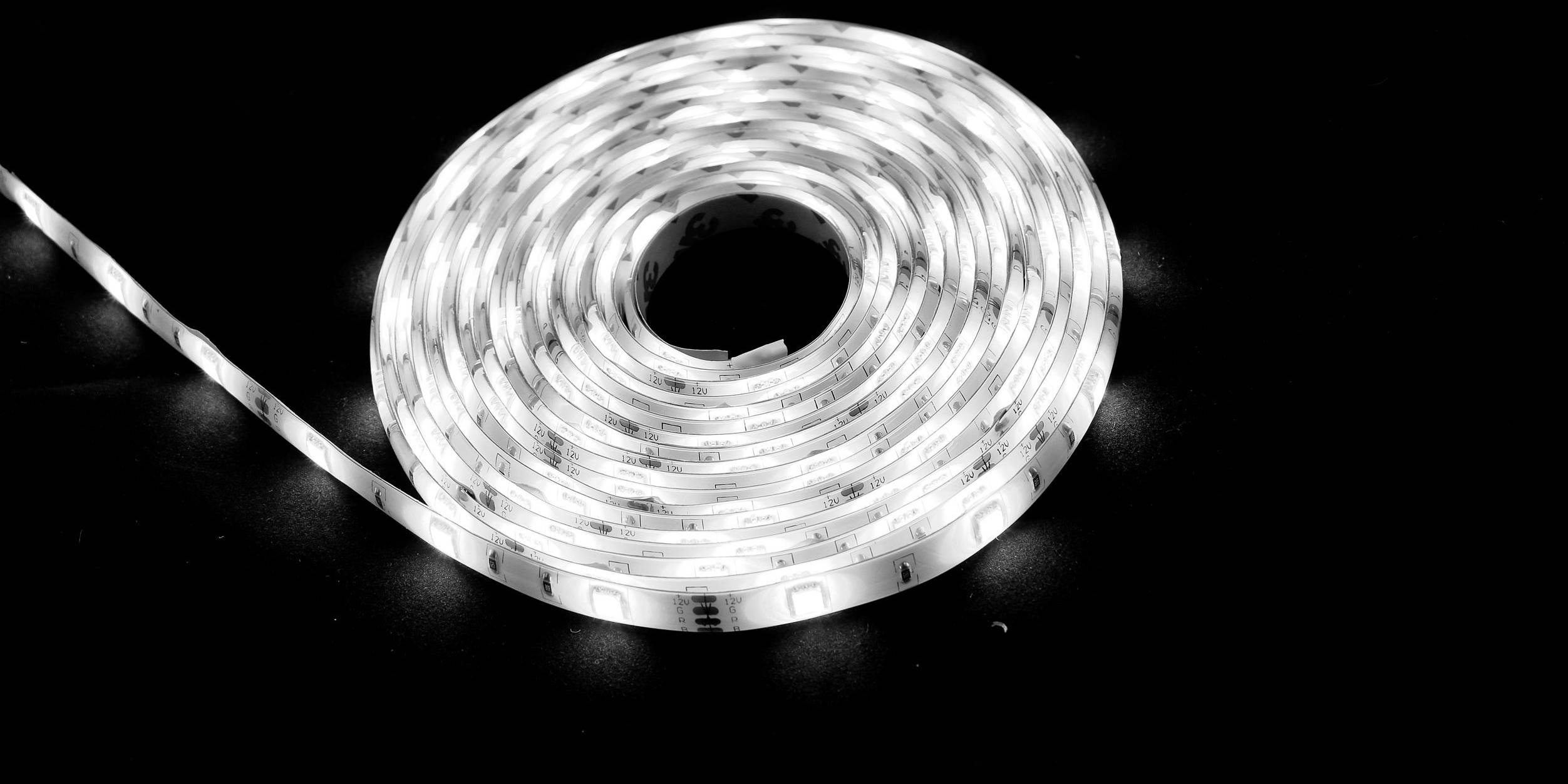 Eine aufgerollte weiße LED-Lichtleiste liegt auf schwarzem Hintergrund.