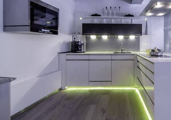 Moderne Küche mit weißen Schränken, eingebautem Ofen, Kaffeemaschine und LED-Leuchten unter den Schränken und am Boden.