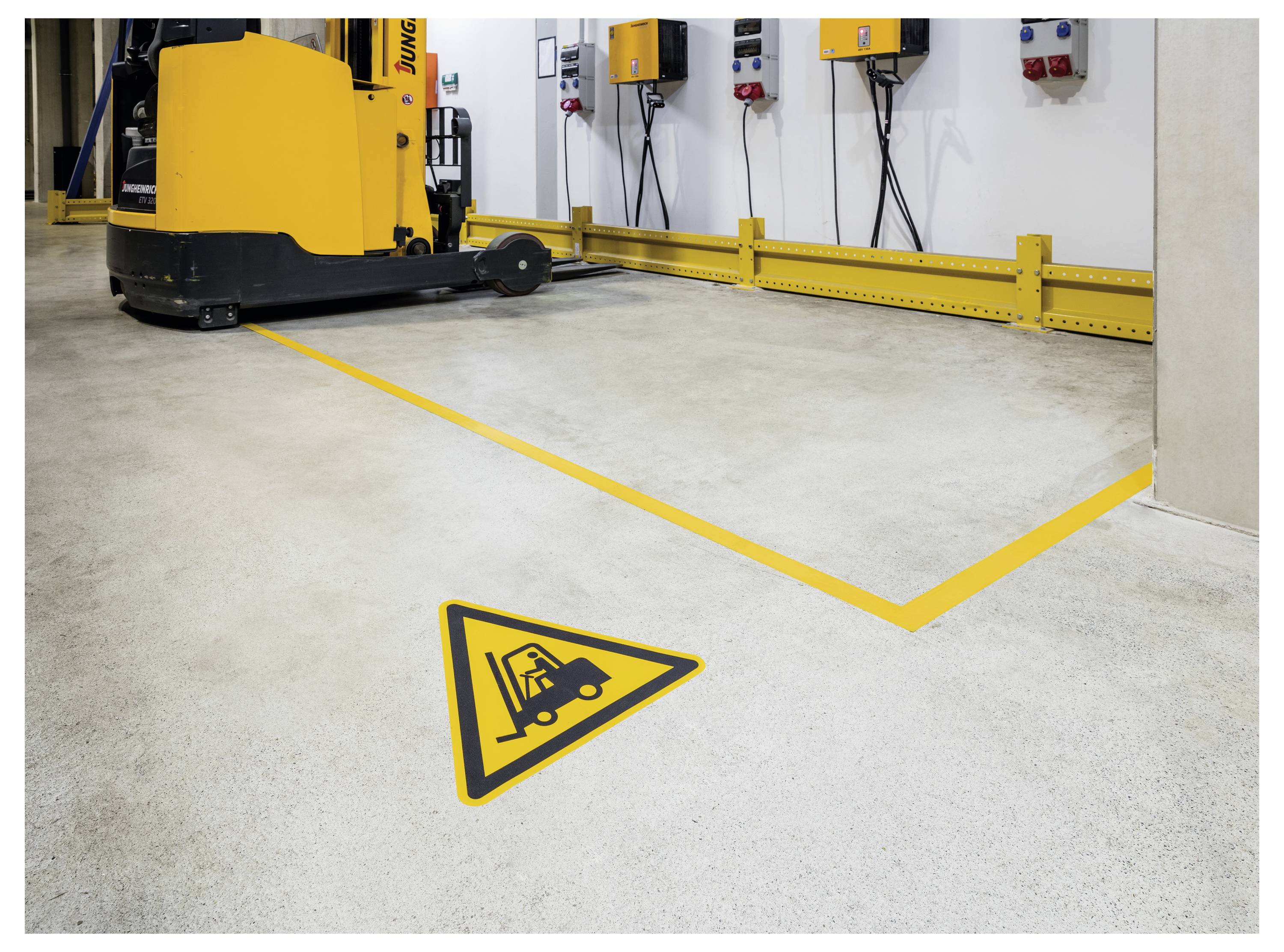 Eine Lagerhalle mit einem gelben Hubwagen nahe einer gelben Sicherheitsmarkierung auf dem Boden, die vor Gefälle warnt.