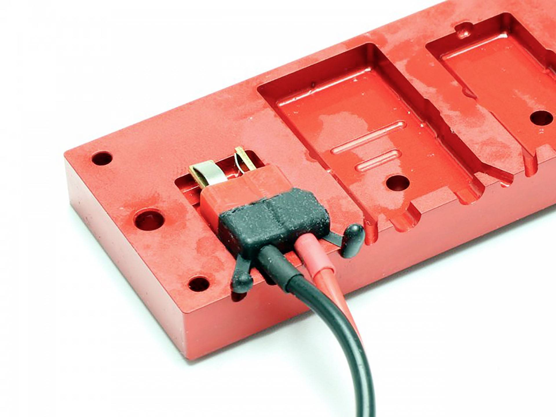 Rotes Stecksystem mit zwei Kabeln angeschlossen an ein rechteckiges Modul, das für industrielle oder technische Anwendungen verwendet wird.