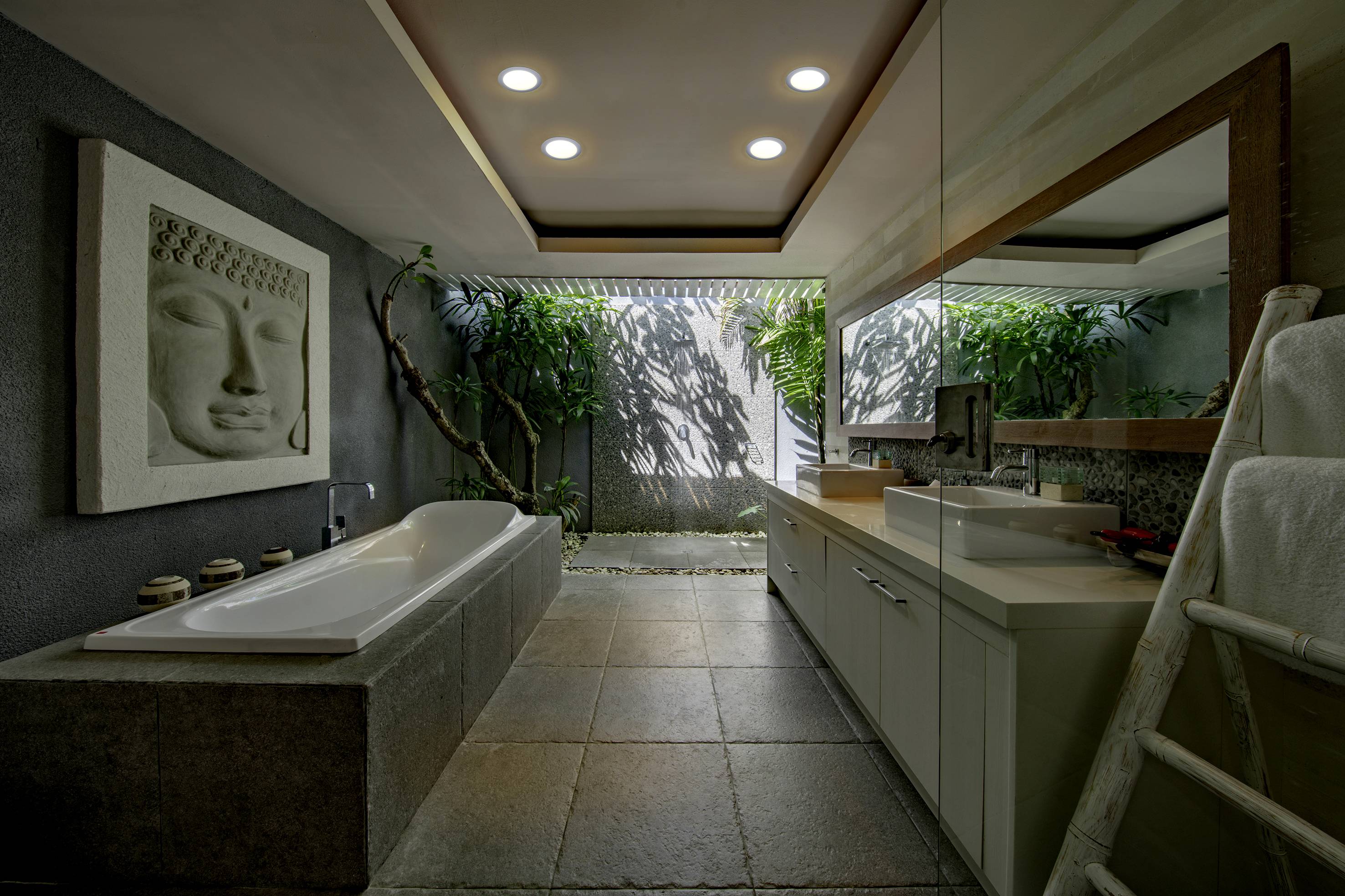 Modernes Badezimmer mit großer Badewanne, Wandkunst und Spiegel; offene Architektur mit Pflanzen, die natürliches Licht hereinlassen.