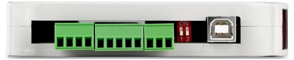 Elektronisches Gerät mit USB-Port, zwei grünen Anschlussklemmen und roten Schaltern. Gerät steht auf einer weißen Fläche.