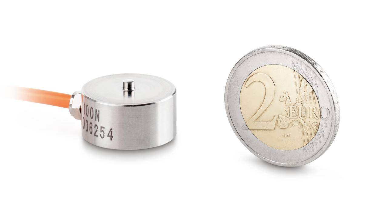 Kleiner runder Sensor links neben einer 2-Euro-Münze zum Größenvergleich. Der Sensor ist aus Metall mit einer Kabelverbindung.