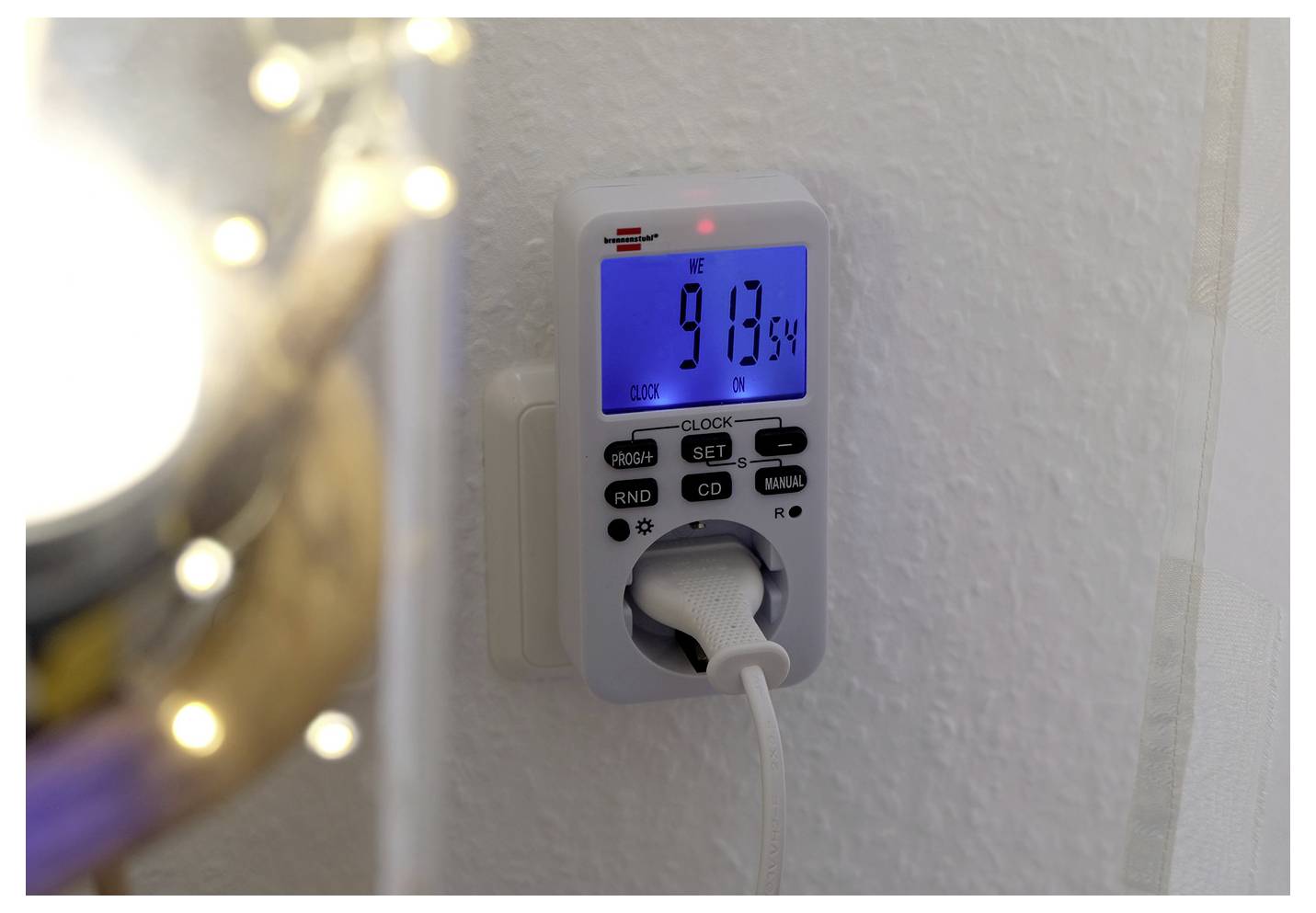 Digitale Steckdosen-Zeitschaltuhr zeigt 21:13:54 Uhr auf einer weißen Steckdose an, mit eingestecktem Kabel.