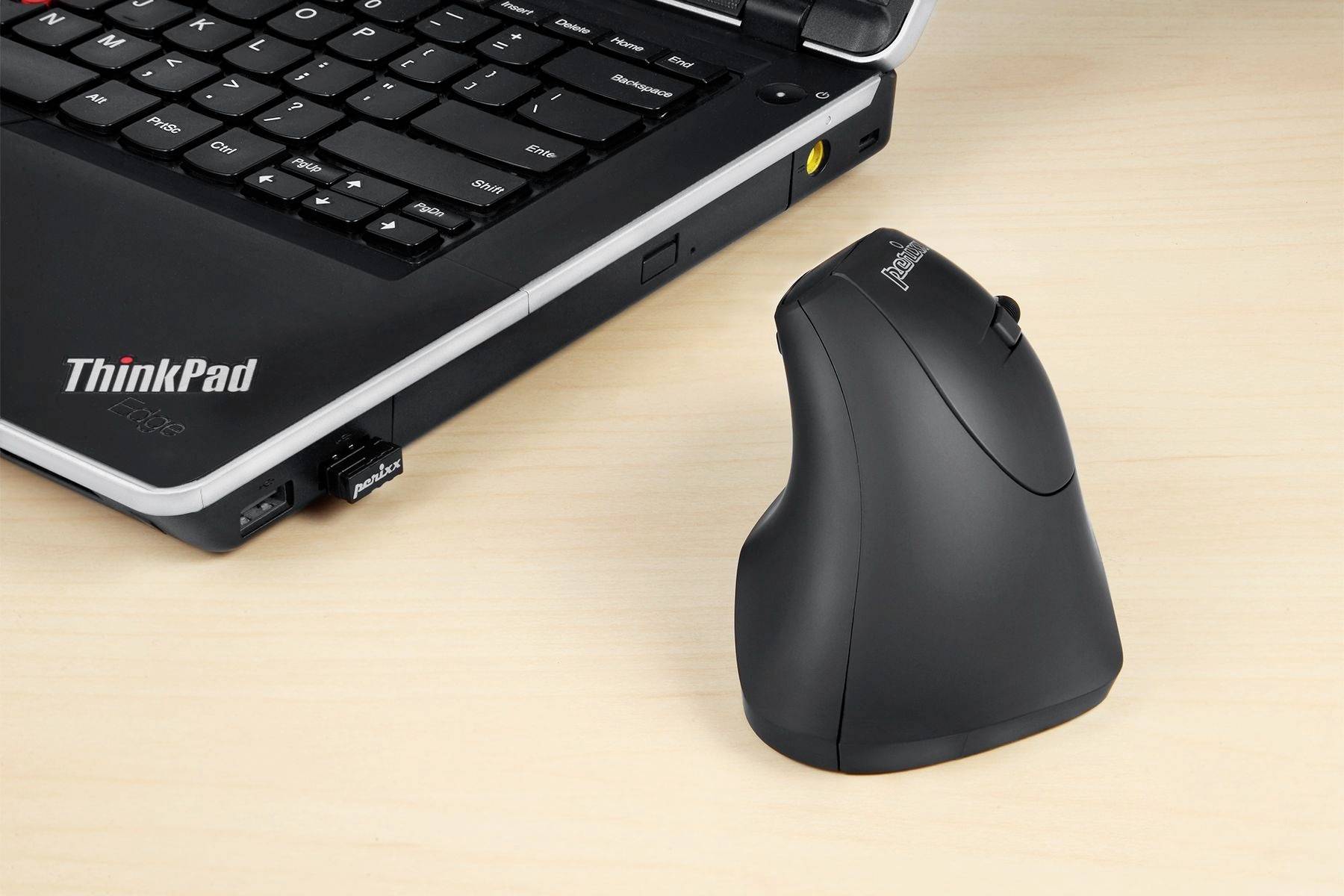 Schwarze, ergonomische Computermaus neben einem aufgeklappten Laptop auf einem Holztisch. Laptop zeigt eine teilweise sichtbare Tastatur.