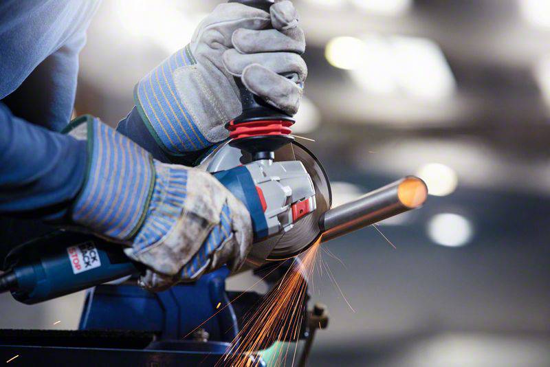 Person schleift Metallrohr mit Winkelschleifer, funken sprühen. Handschuhe und Schutzkleidung vermitteln Sicherheit bei der Arbeit.