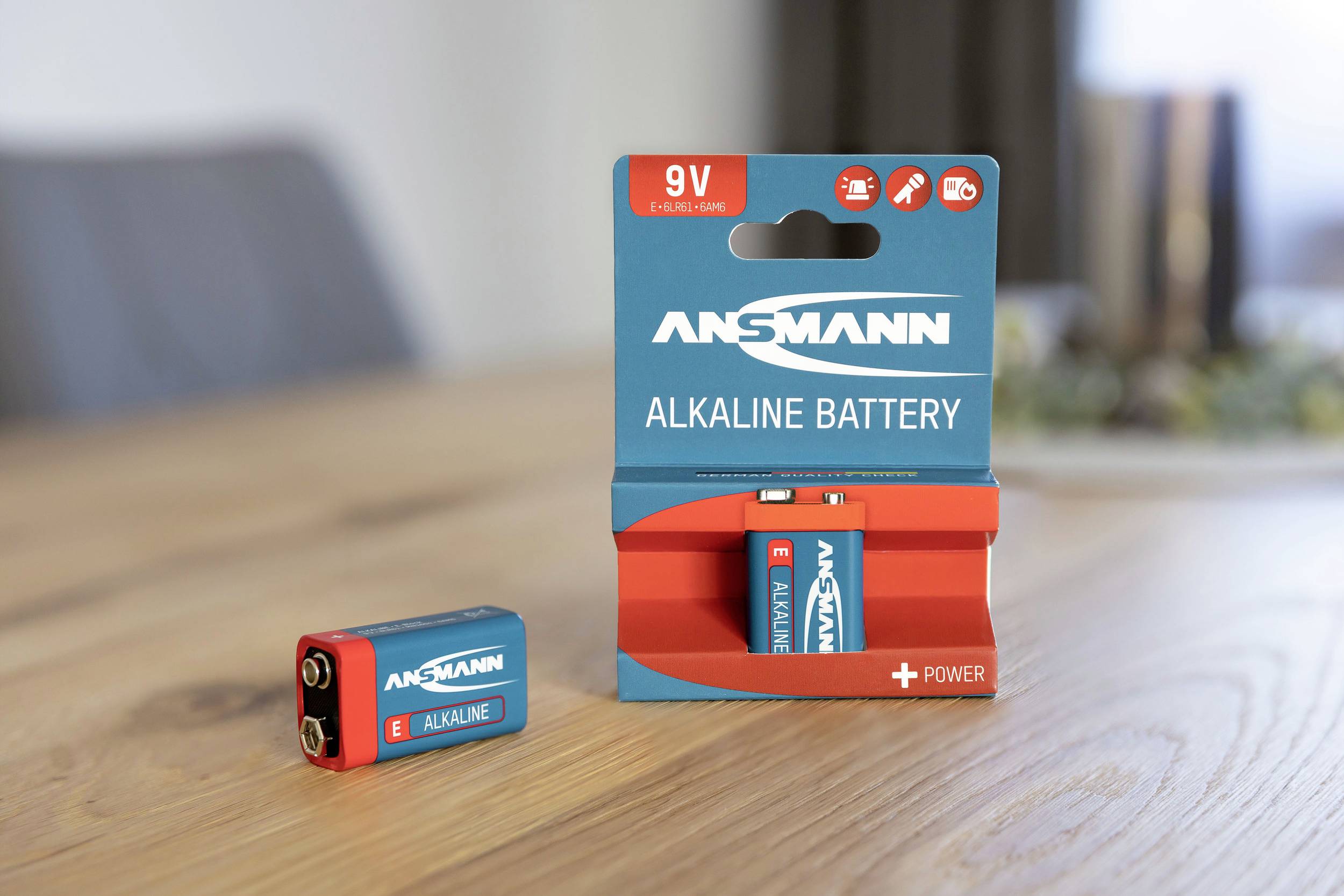 Eine Ansmann 9V Alkalibatterie steht neben ihrer Verpackung auf einem Holztisch.