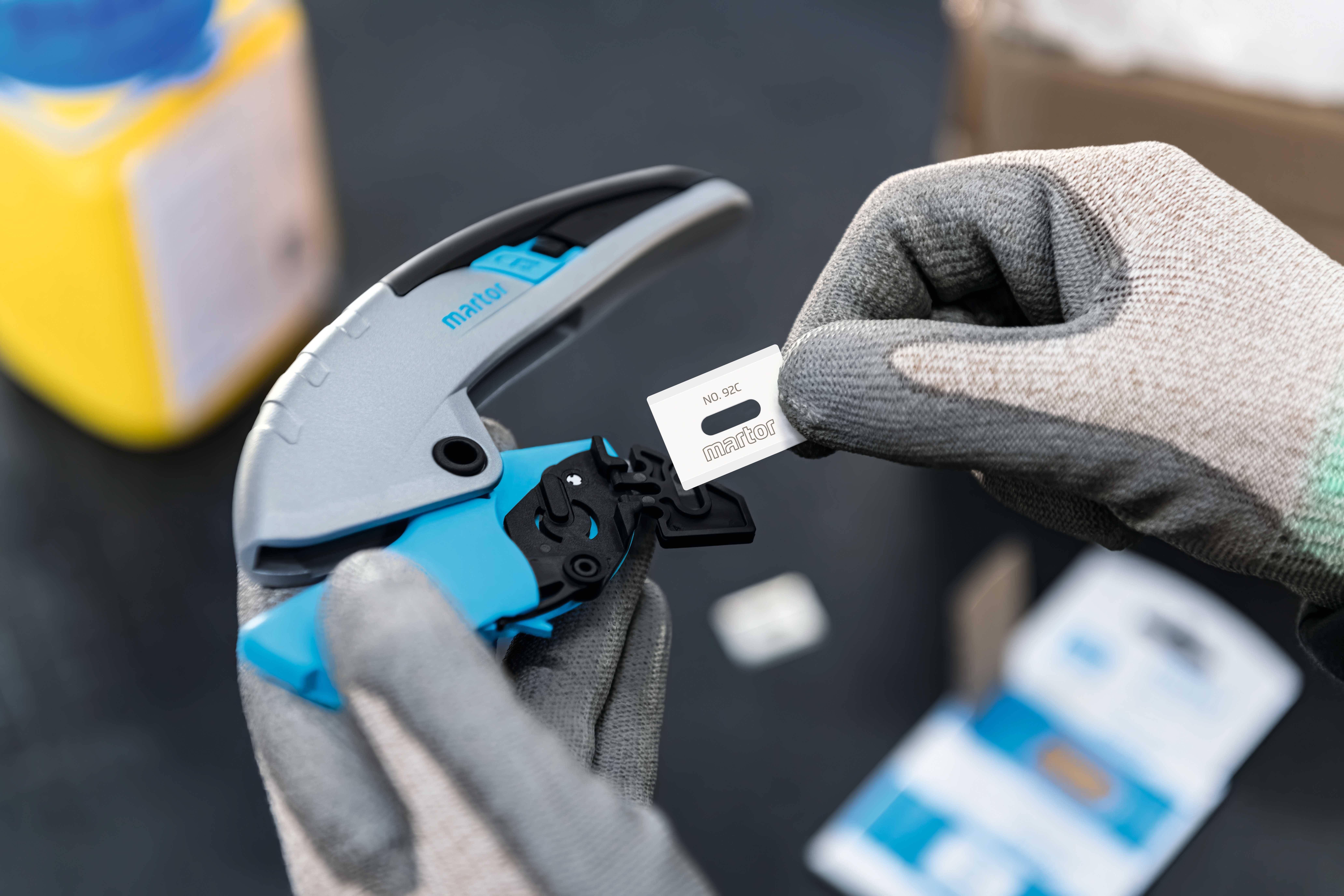 Person trägt Handschuhe und hält ein Werkzeug in der linken Hand. In der rechten Hand wird ein Etikett mit der Aufschrift 'NO.16' gehalten.