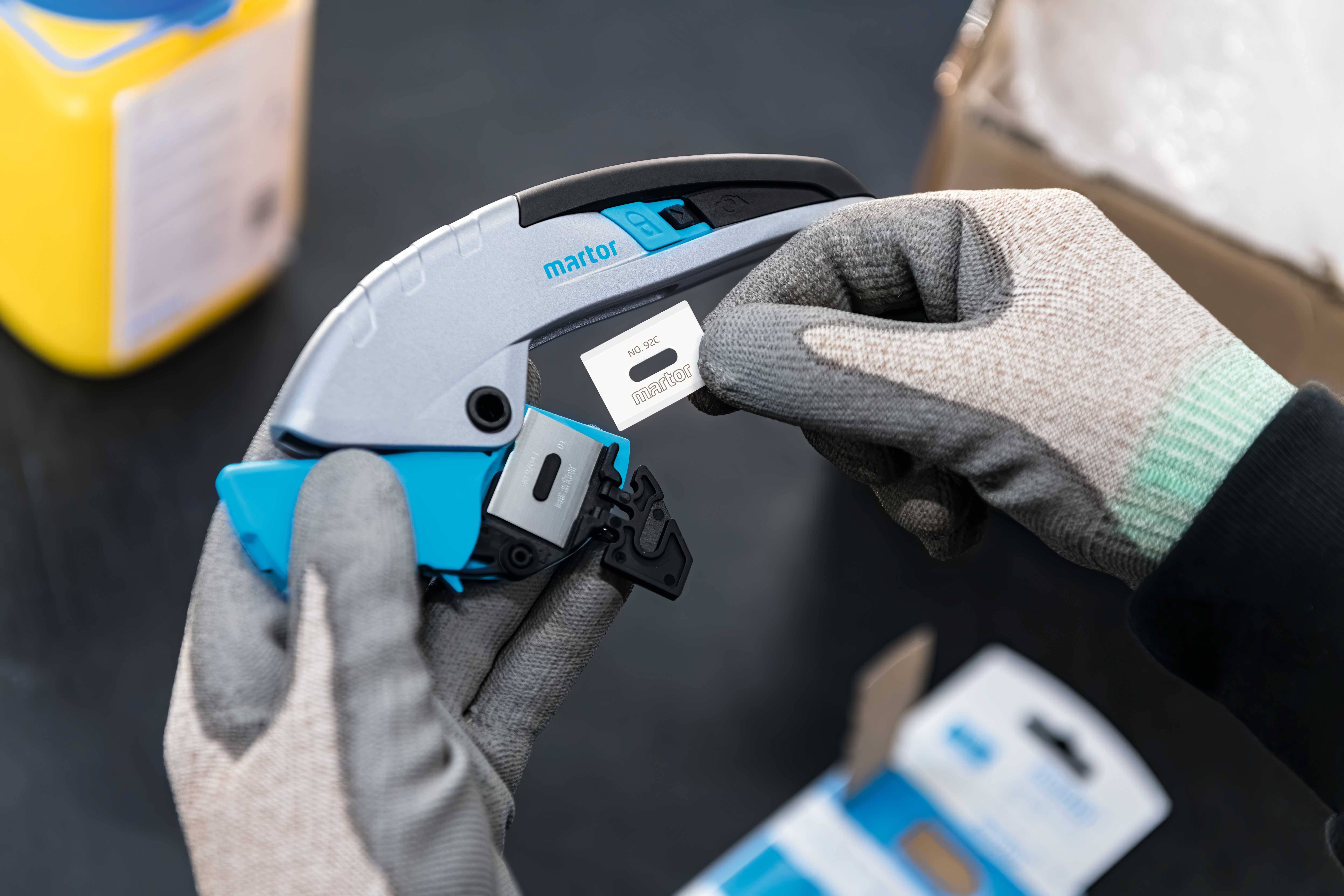 Person mit Handschuhen hält ein graues und blaues Gerät und platziert ein kleines weißes Etikett mit schwarzem Text darauf.