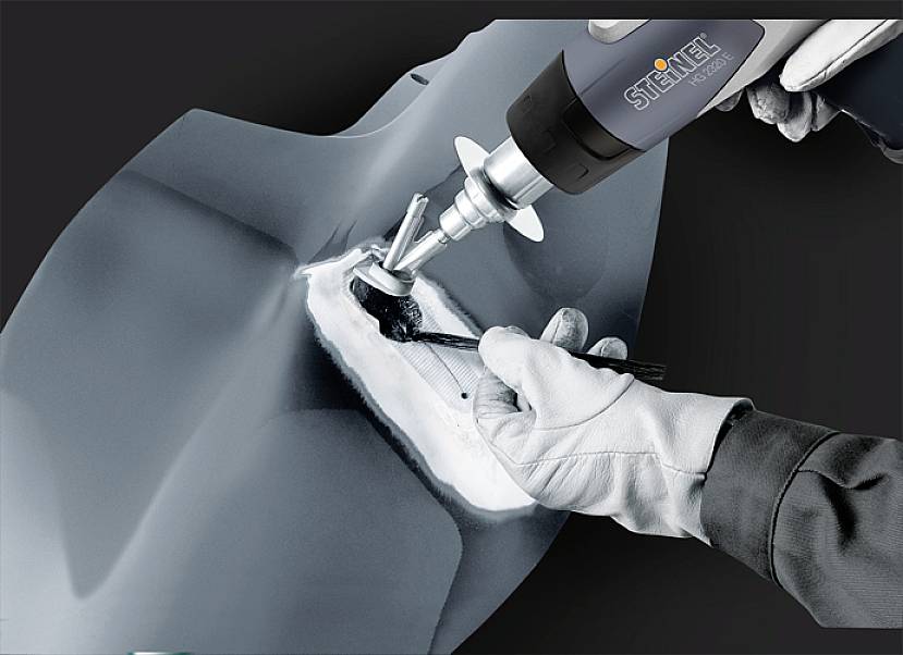 Eine Person trägt Handschuhe und poliert eine metallische Oberfläche mit einem Elektrowerkzeug, um sie zu glätten und zu bearbeiten.