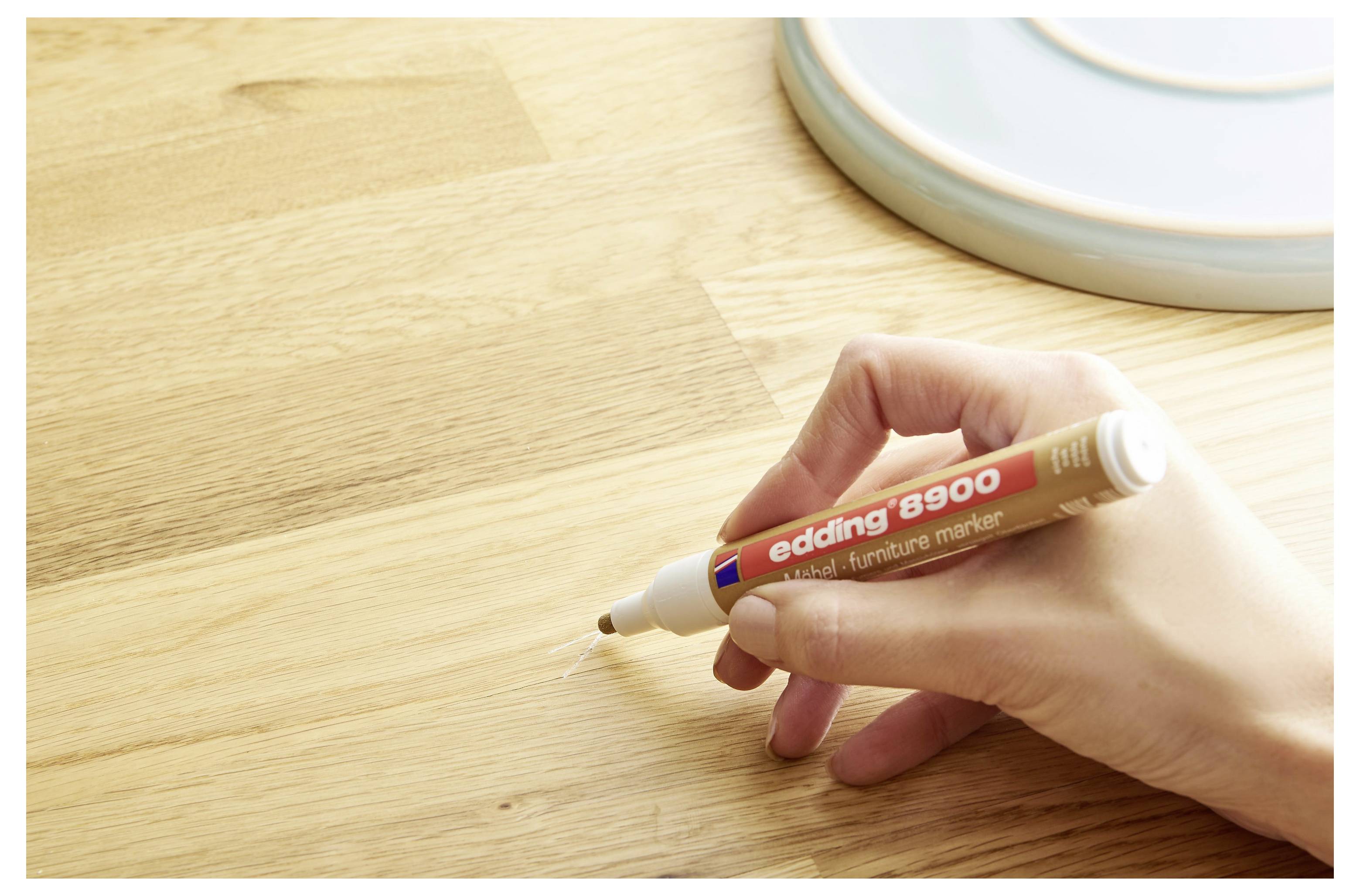 Hand, die einen braunen Möbelmarkerstift verwendet, um einen Kratzer auf einer Holztischplatte zu retuschieren.