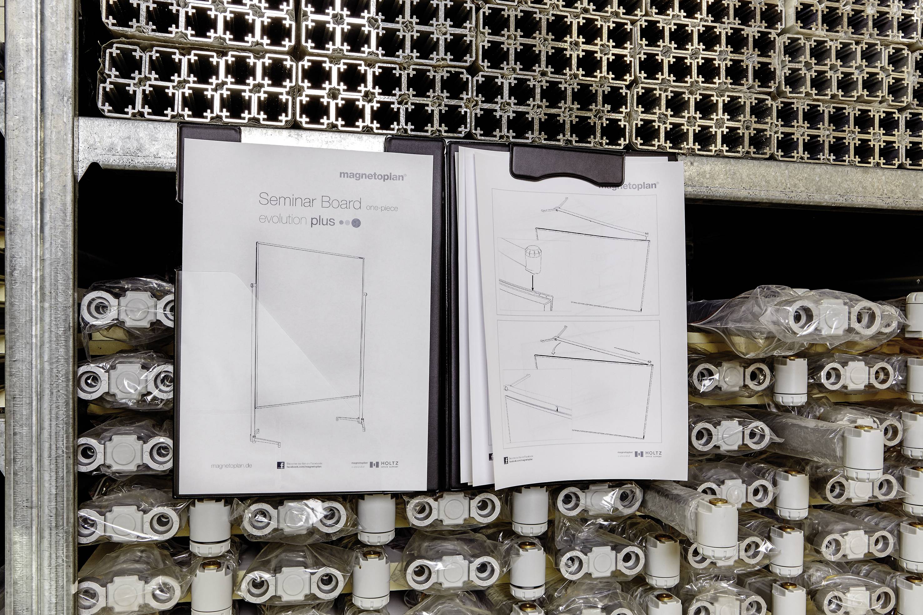 'Metallregal mit zahlreichen Verpackungen, darunter ein Produktblatt von 'Seminar Board evolution plus' mit Skizzen und Hinweisen.'
