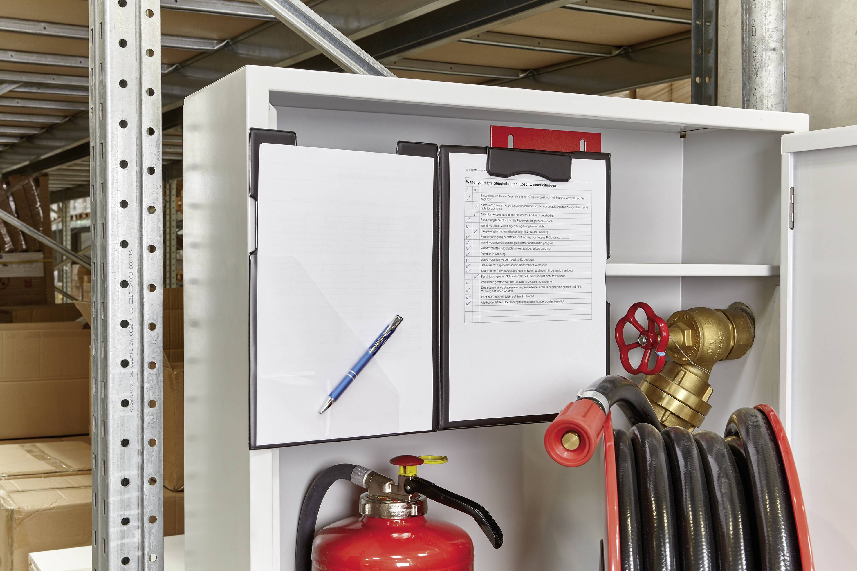 Ein offener Schrank zeigt einen Feuerlöscher, einen Wasserschlauch mit Armatur und Befestigungen sowie ein Klemmbrett mit Papier.