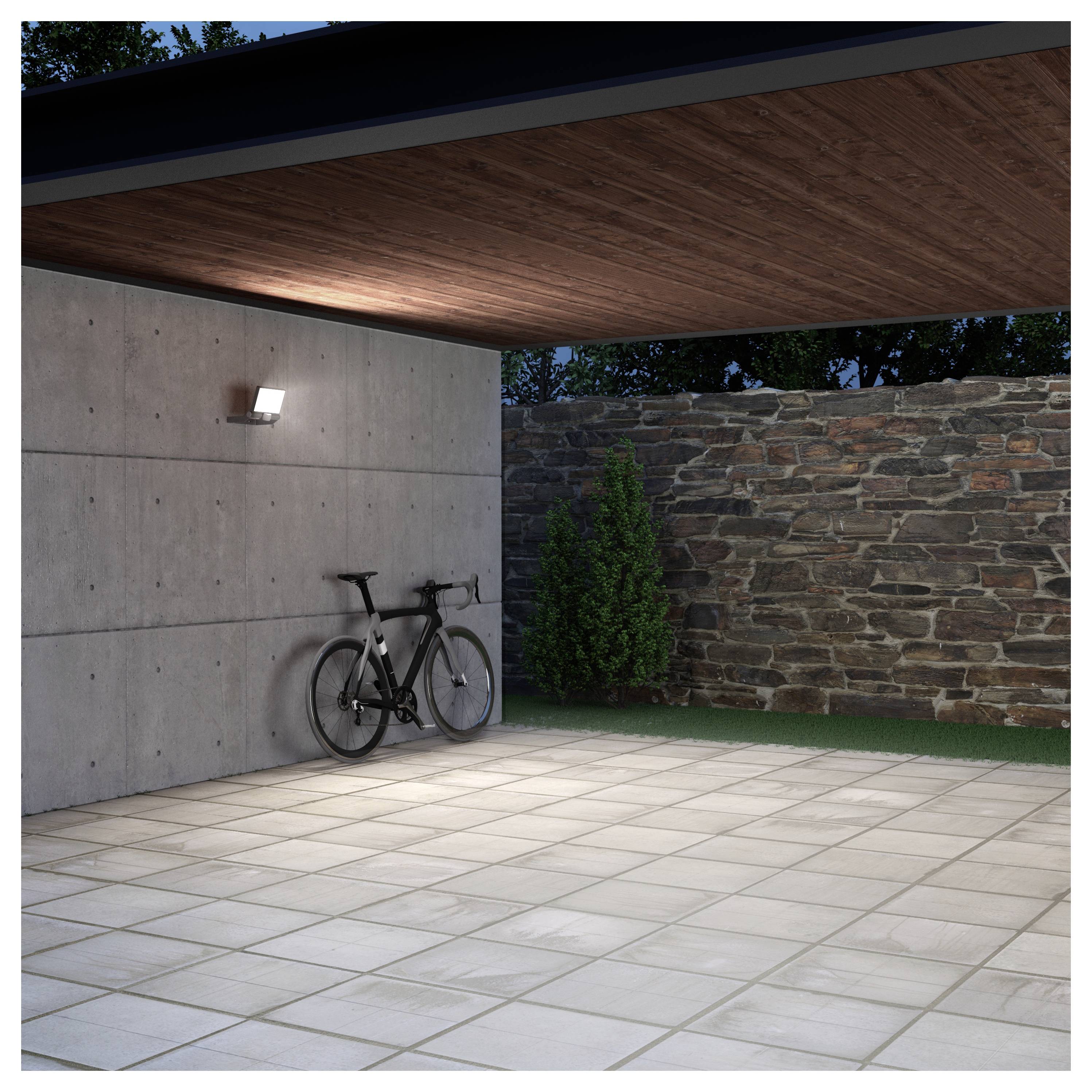 Moderner überdachter Patio mit Fliesenboden, Betonwand, Steinmauer und einem Fahrrad unter einem Holzpaneel-Dach in der Dämmerung.