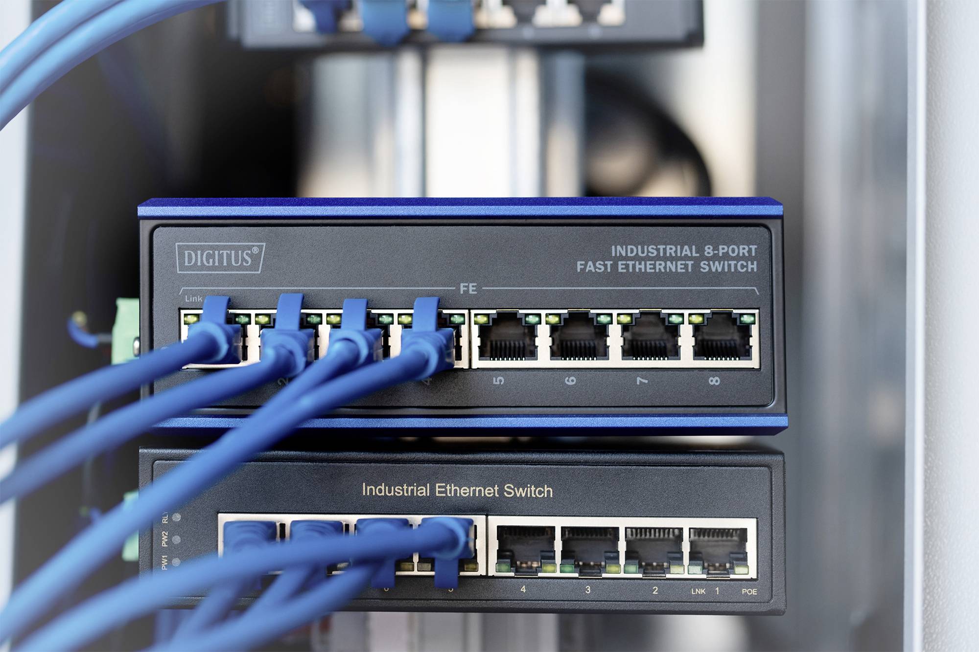 Zwei Netzwerk-Switches mit mehreren eingesteckten Ethernet-Kabeln; oberer Switch ist ein 8-Port Fast Ethernet Switch, der untere ein Industrial Ethernet Switch.