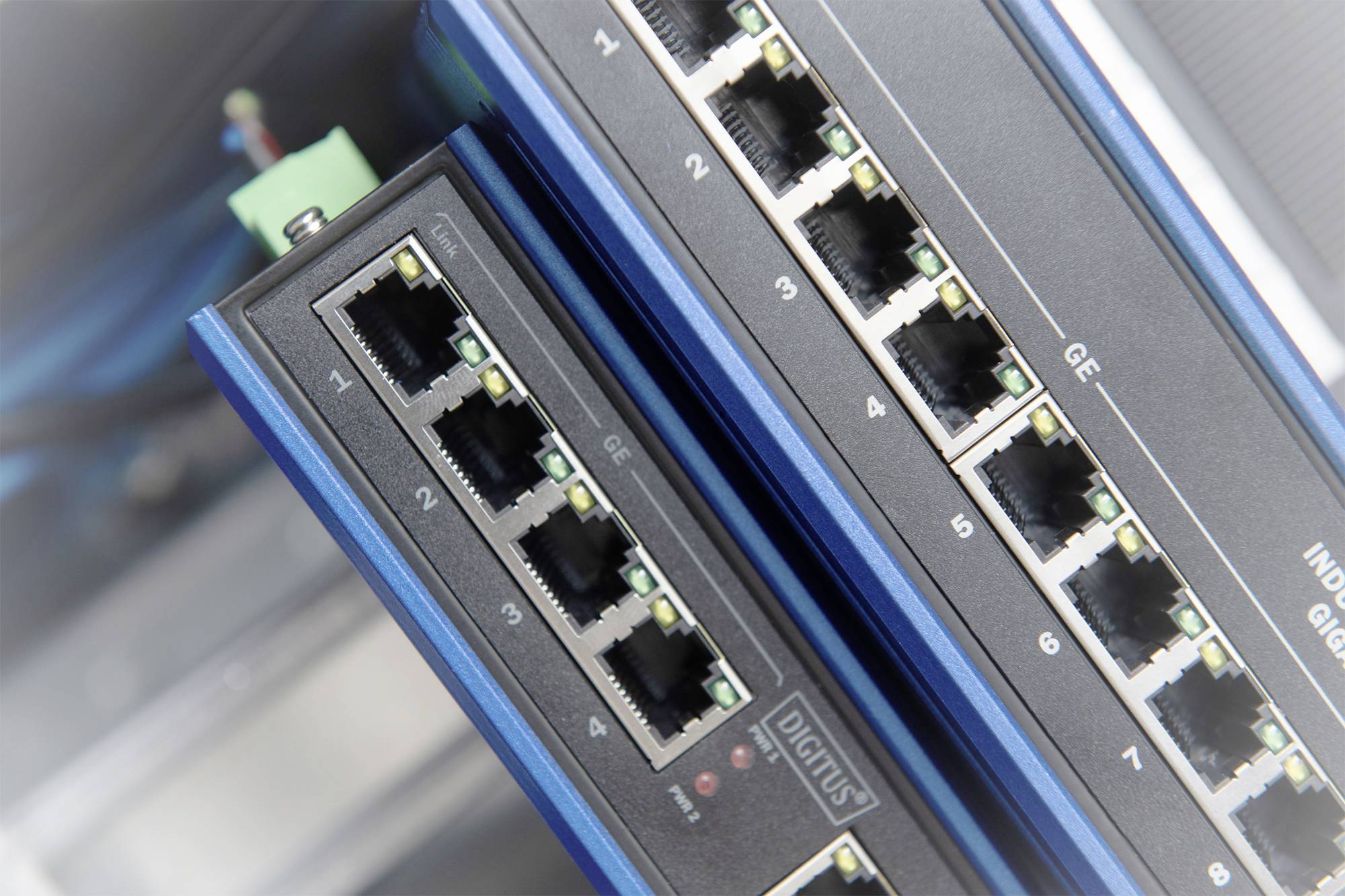 Zwei Netzwerk-Switches mit mehreren Ethernet-Ports, gekennzeichnet mit 'GE'. Sie sind in einem Serverraum installiert und verbunden.
