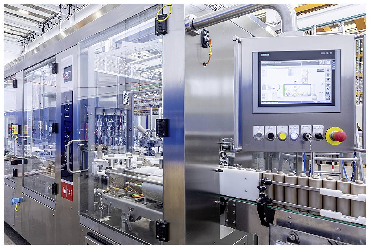 Eine industrielle Verpackungsmaschine mit Touchscreen-Bedienfeld in einer modernen Fabrikumgebung. Röhrenförmige Produkte auf einem Förderband.