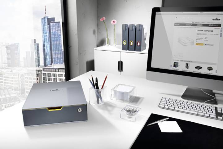Ein modernes Büro mit Blick auf eine Stadt. Im Vordergrund stehen ein Monitor mit einem geöffneten Website-Shop, eine Tastatur und Organisationsmaterialien.