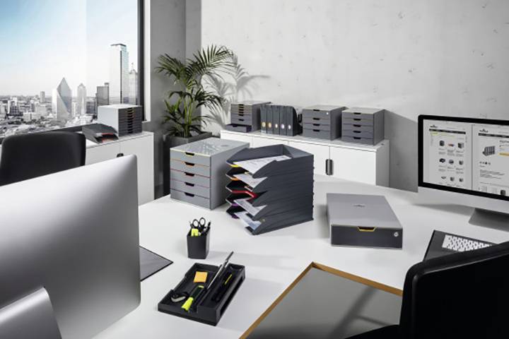 Ein modernes Büro mit Blick auf die Stadt. Auf dem Schreibtisch stehen Computerbildschirme, Ablagefächer und Büromaterialien.