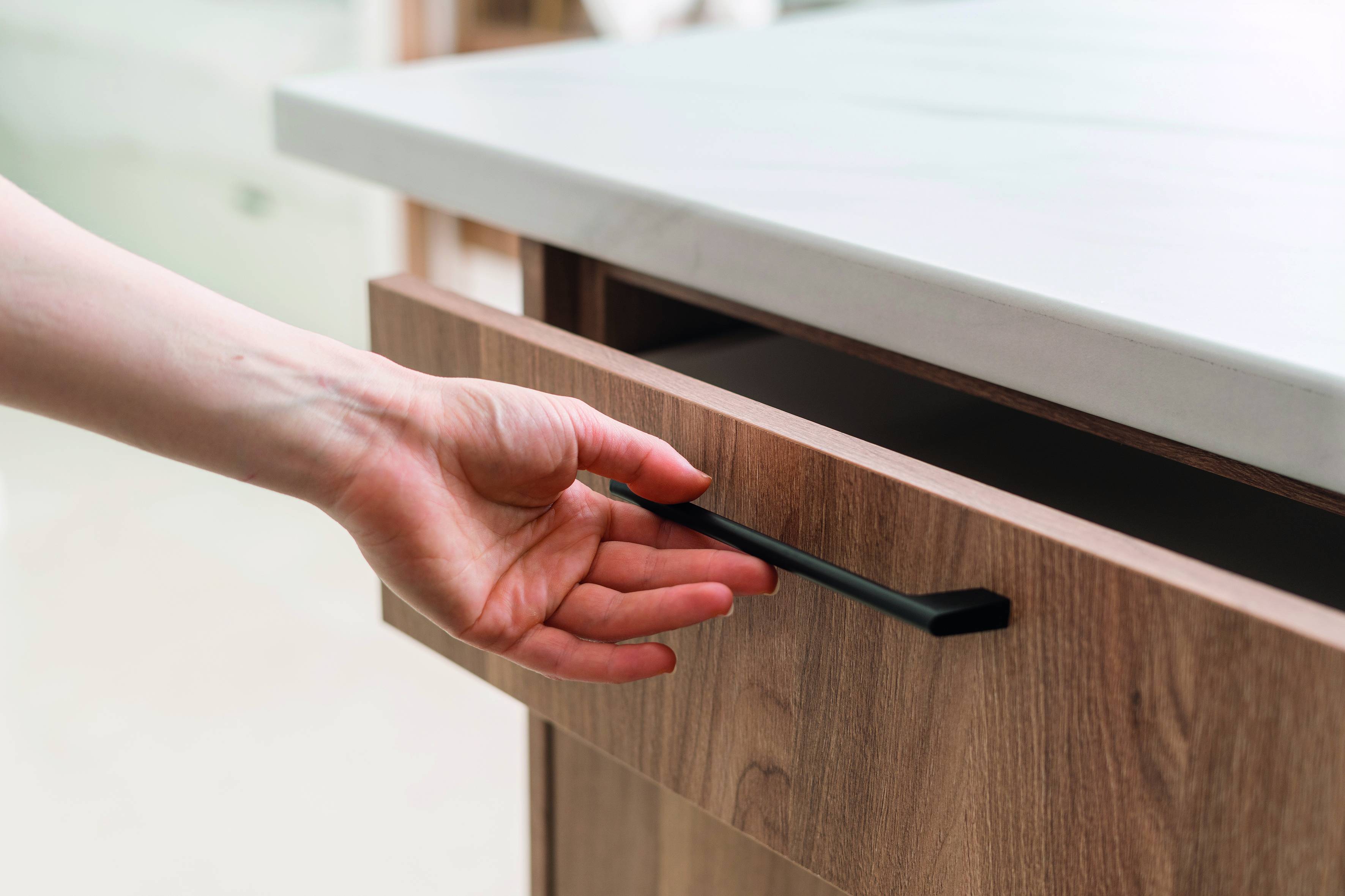 Eine Hand schaltet das ausziehbare Unterschranklichtsystem eines modernen Schranks ein und erleuchtet den Schubladenbereich in einer Küche oder einem Arbeitsbereich.