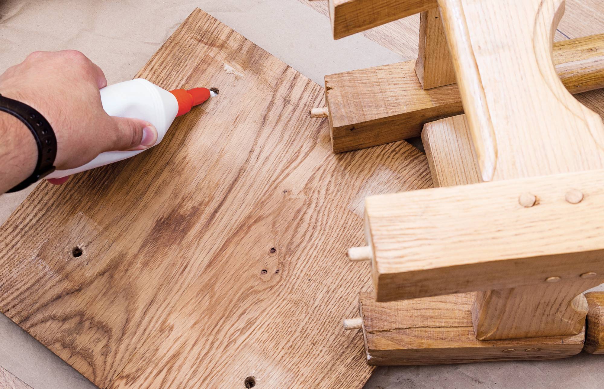 Eine Hand trägt Holzleim auf ein Brett mit Dübeln auf und montiert eine Holzmöbelverbindung.