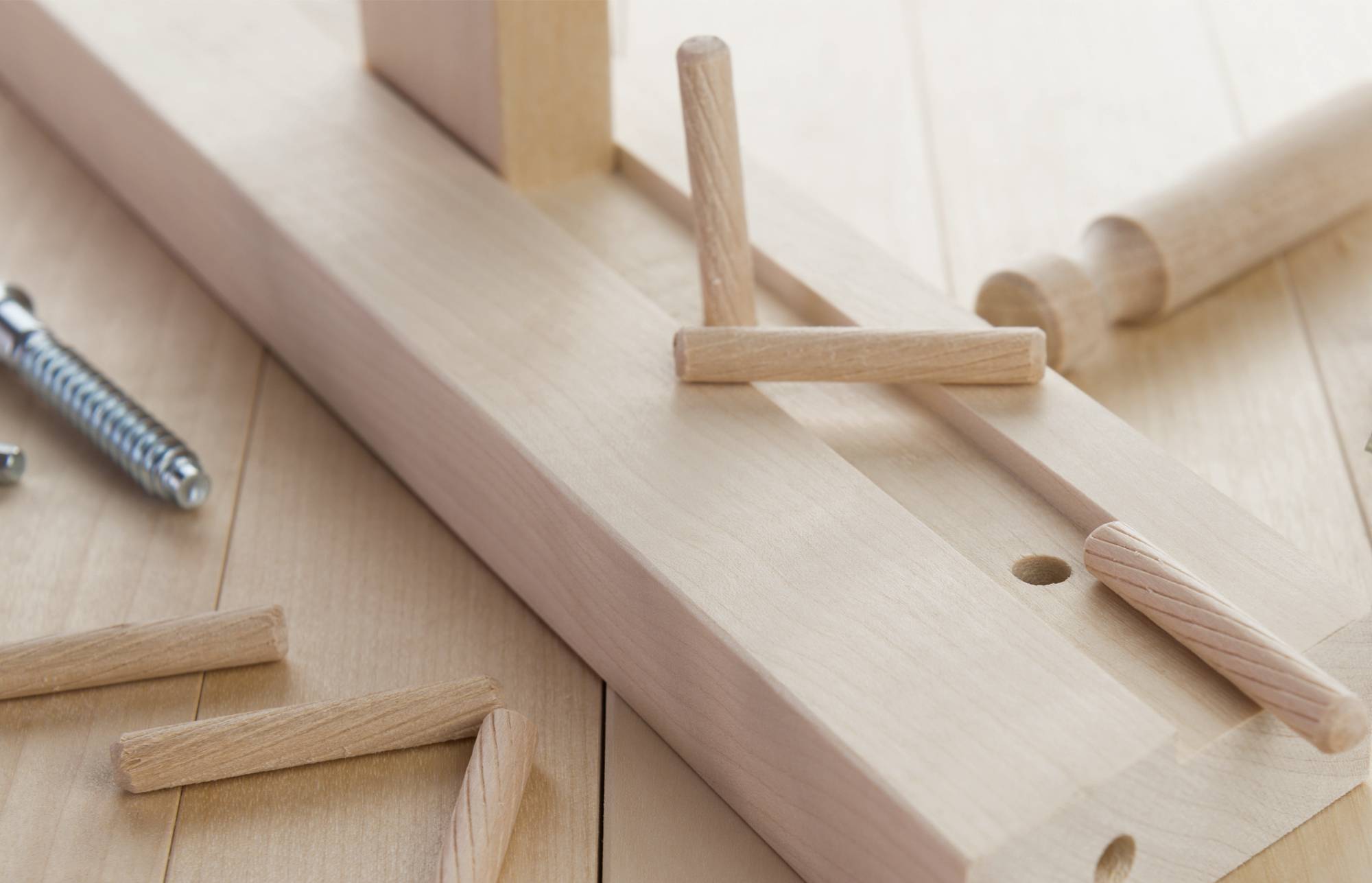 Nahaufnahme eines Holzbearbeitungswerkzeugs: Eine Holzvorrichtung mit Dübeln und einer Federspannzwinge auf einer hellen Holzwerkbank.