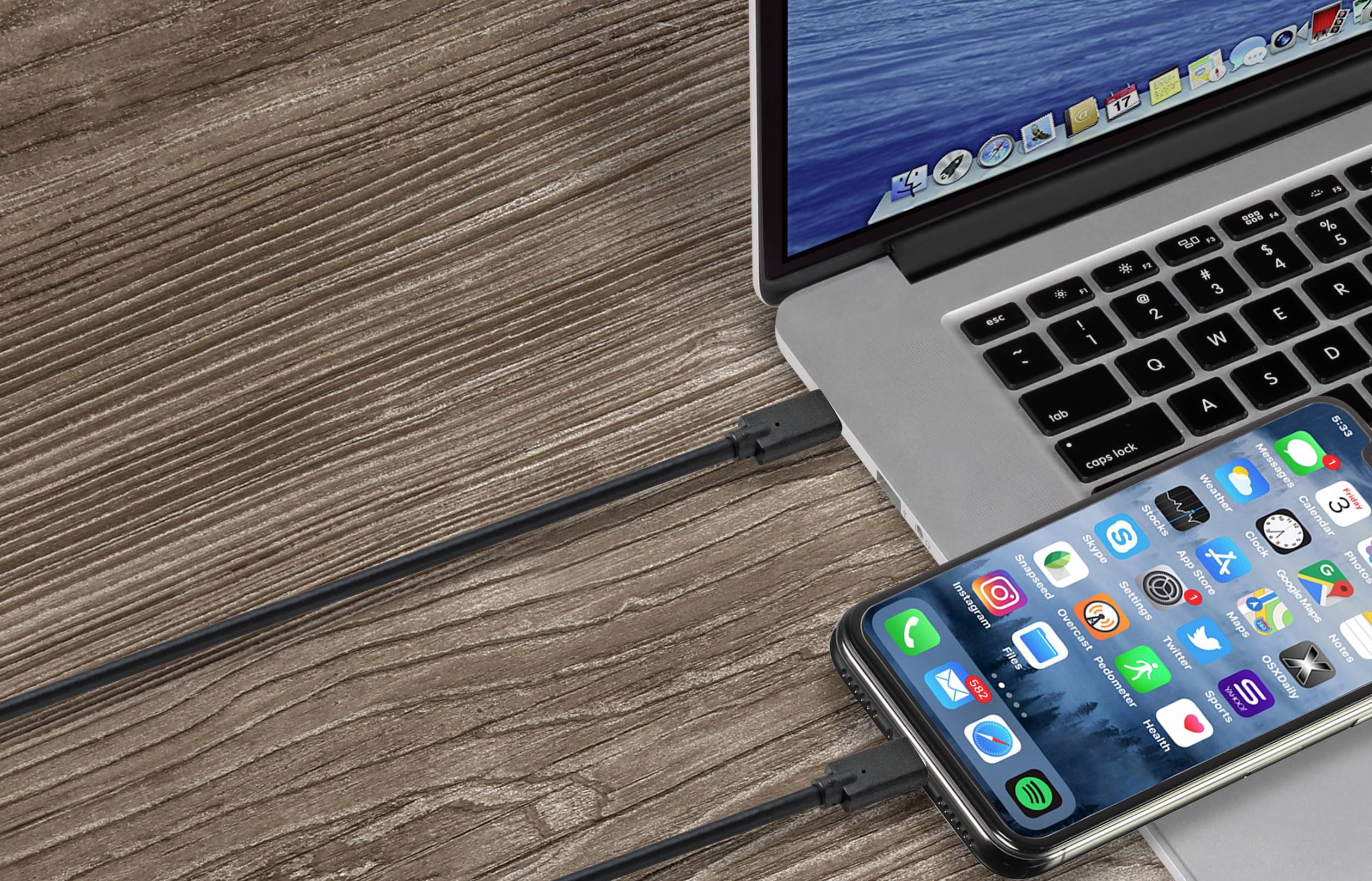 Ein Laptop und ein Smartphone sind über USB-Kabel verbunden, die auf einem Holztisch liegen.