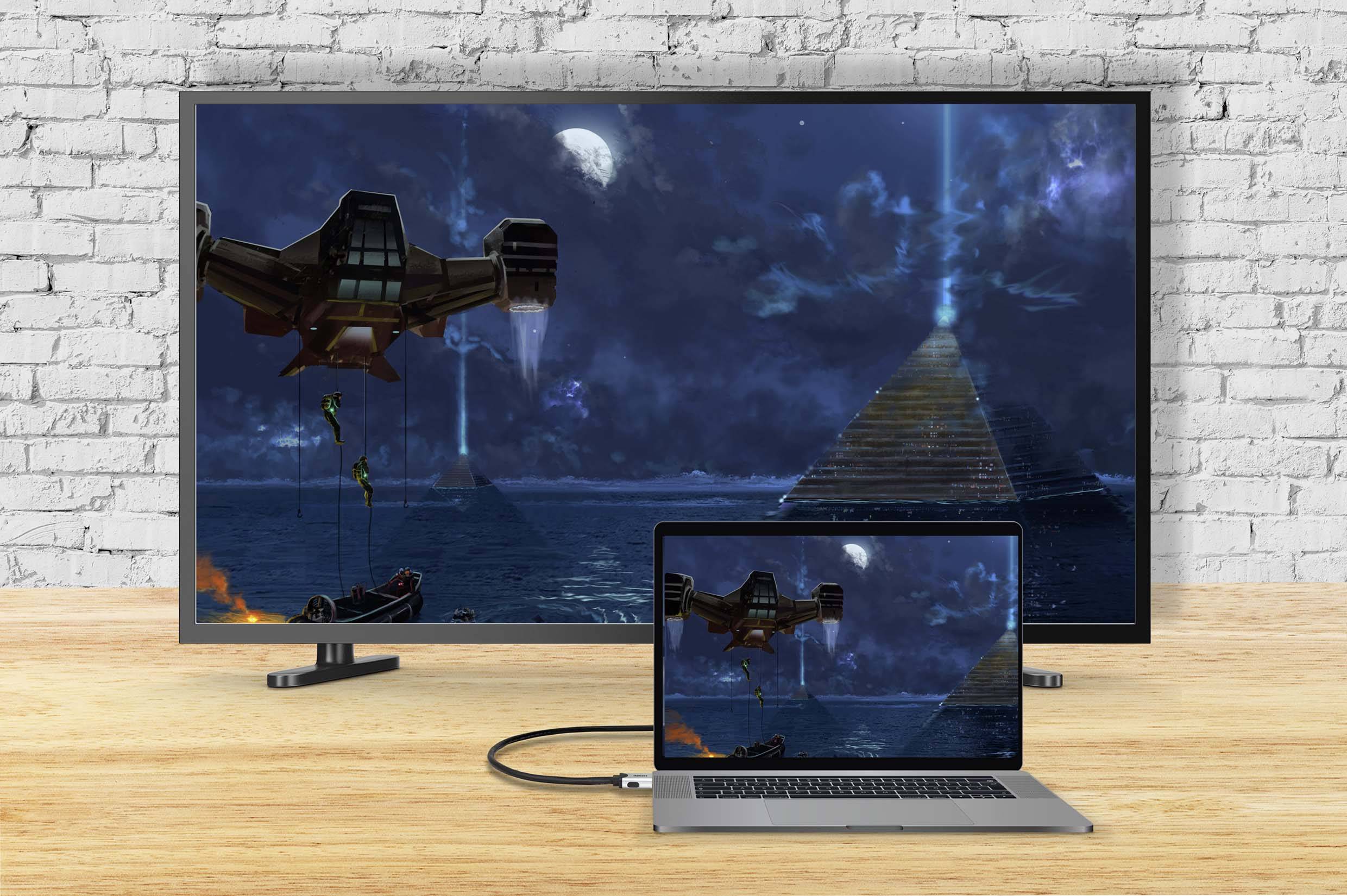 Ein Laptop ist über ein Kabel mit einem großen Fernseher verbunden. Auf beiden Bildschirmen ist ein Bild von einem Raumschiff über einem Meer vor einer Pyramide zu sehen.
