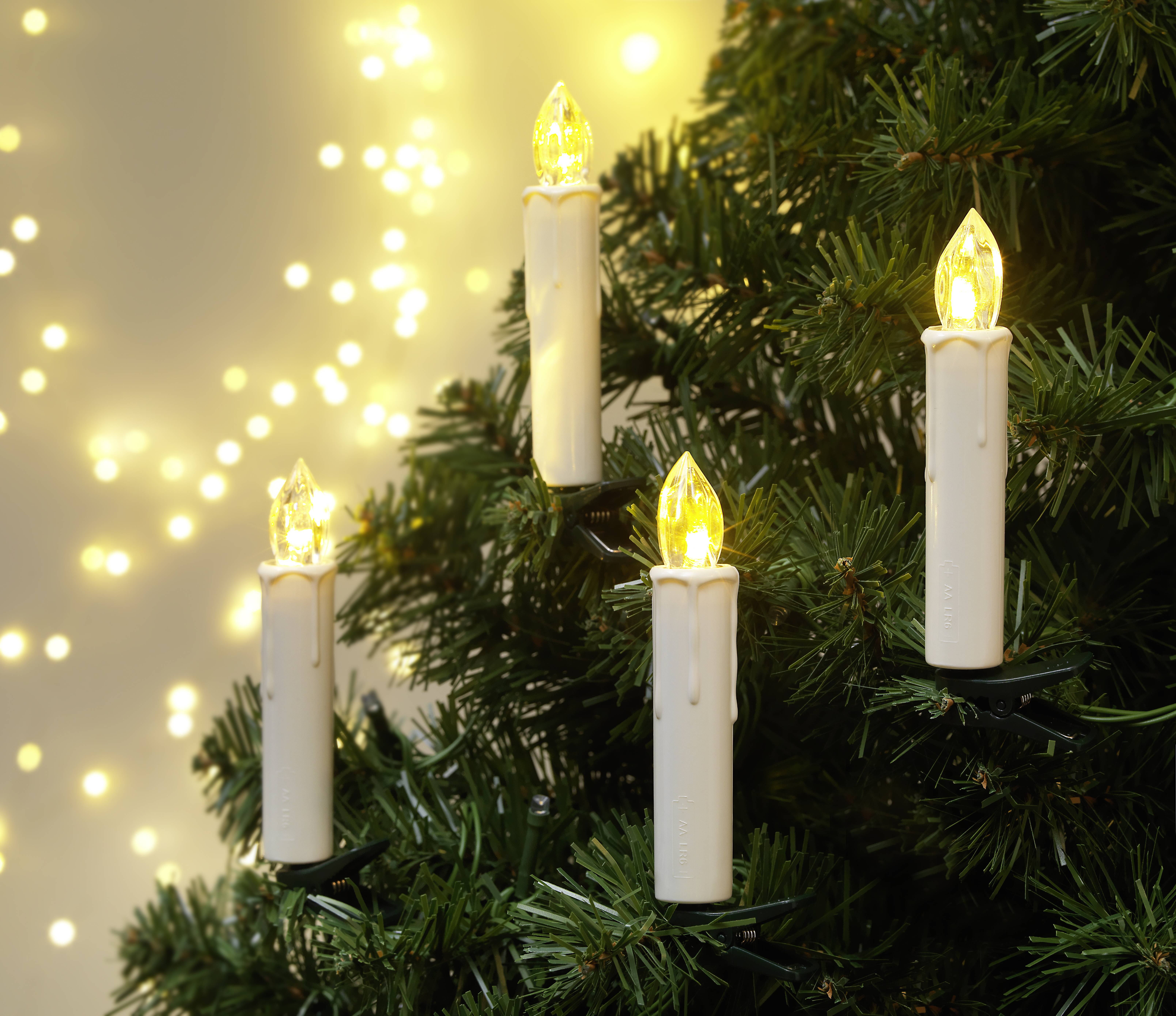 Fünf elektrische Kerzen mit warmem Licht auf einem Tannenbaum, umgeben von verschwommenen Lichtern im Hintergrund. Stimmungsvoll und festlich.