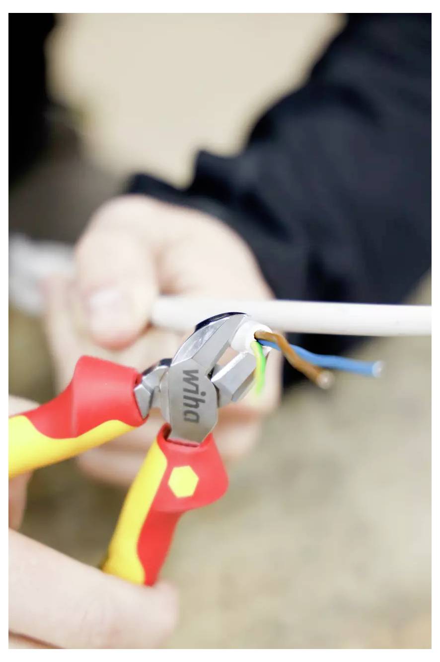 Hände, die einen Drahtschneider verwenden, um elektrische Drähte zu abisolieren und die farbigen inneren Drähte freizulegen.