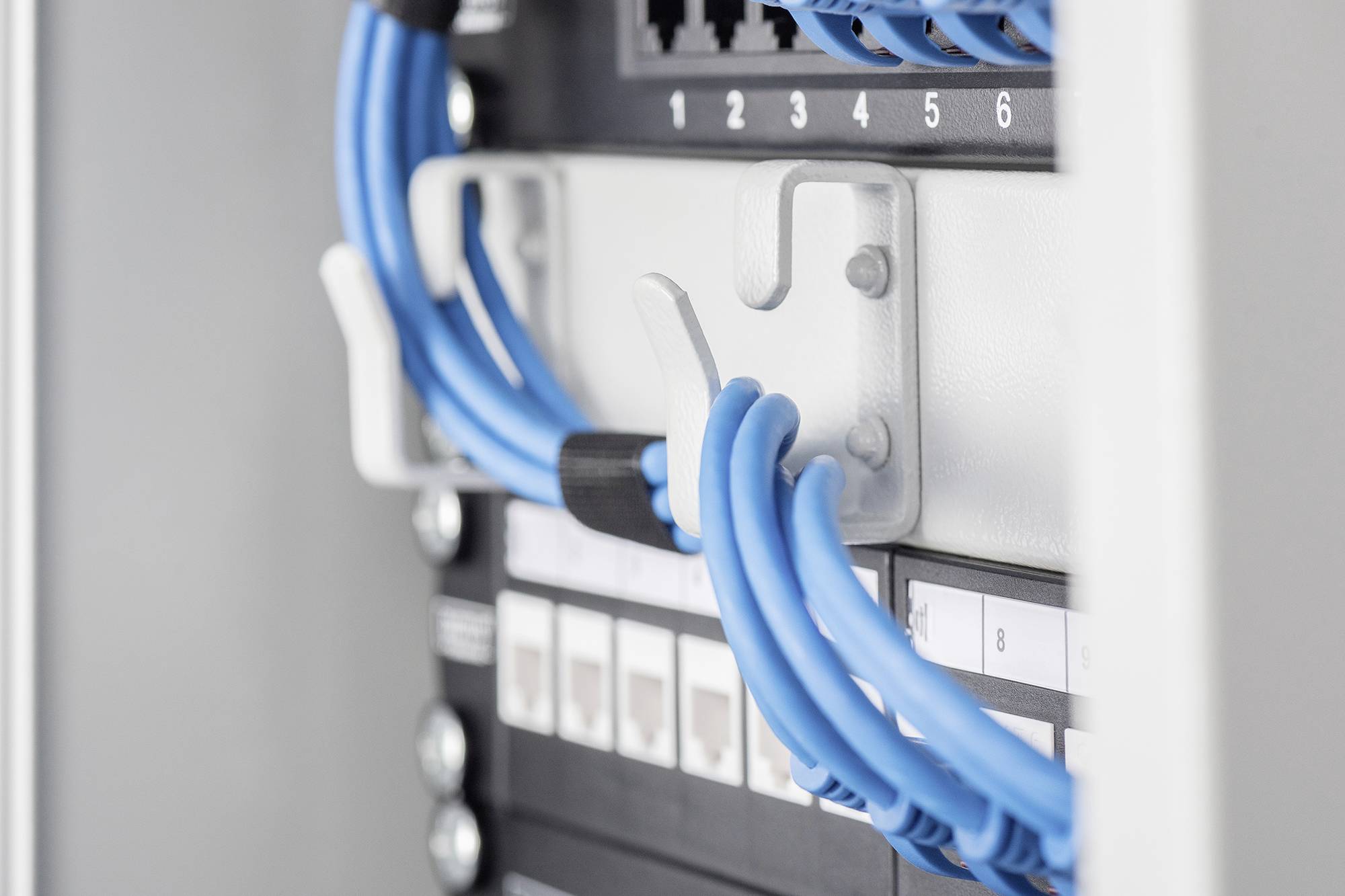Blauer Netzwerkkabelstrang in einem Kabelorganisator an einem Patchpanel. Mehrere Ethernet-Ports und nummerierte Schalter sichtbar.
